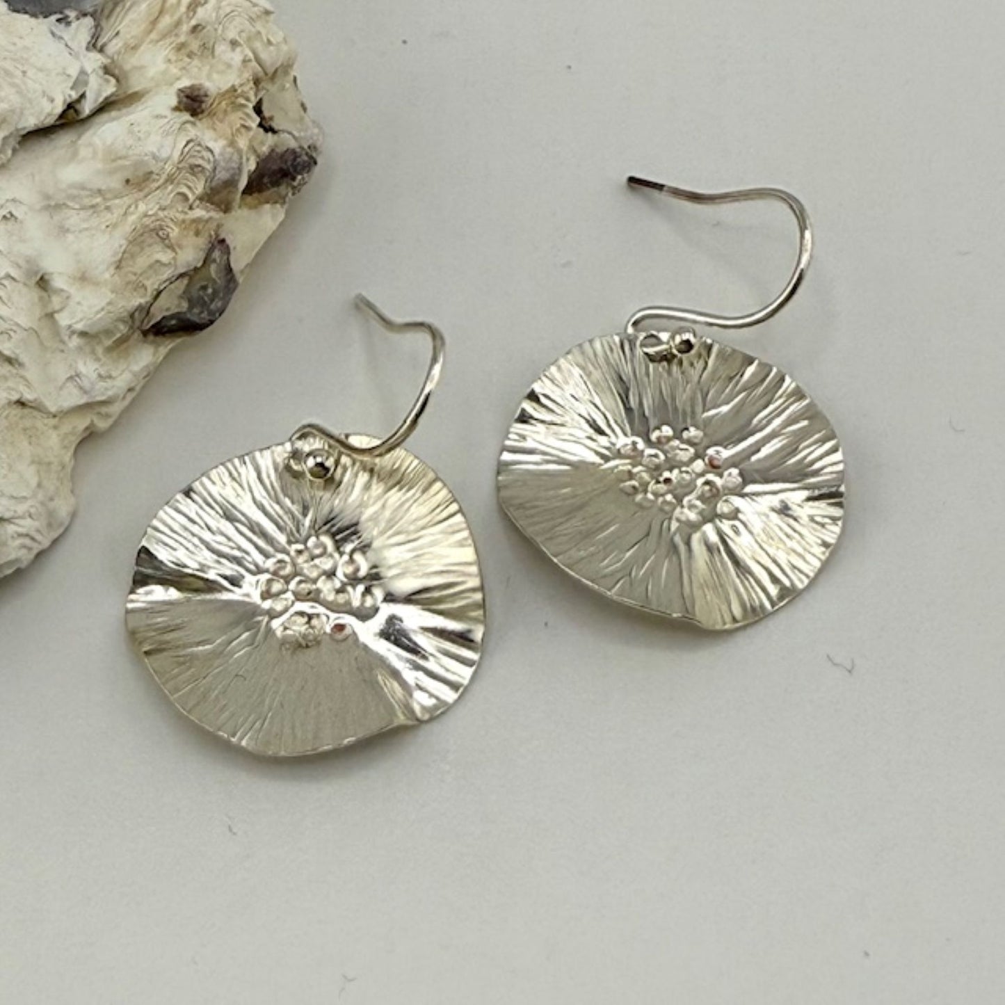 Silver floral earrings on a light gray surface with a natural stone background