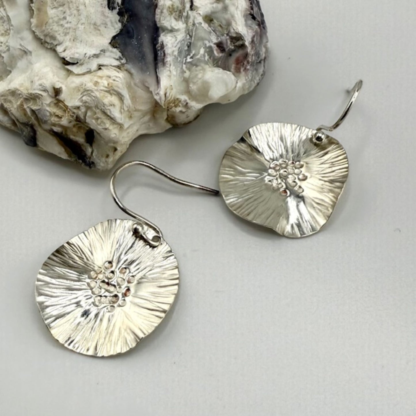 Silver earrings with textured design on a light gray background