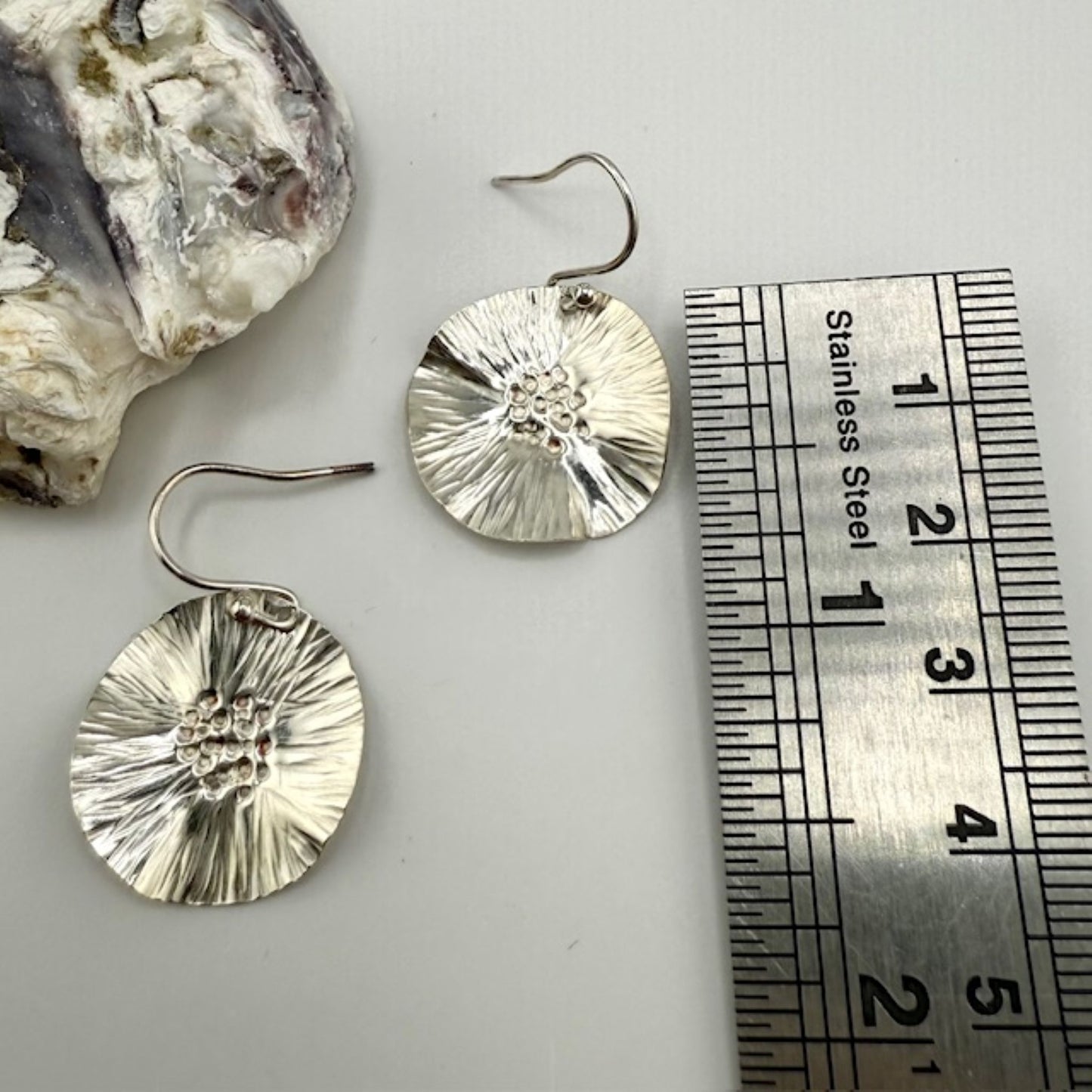 Silver flower earrings next to a ruler on a white background