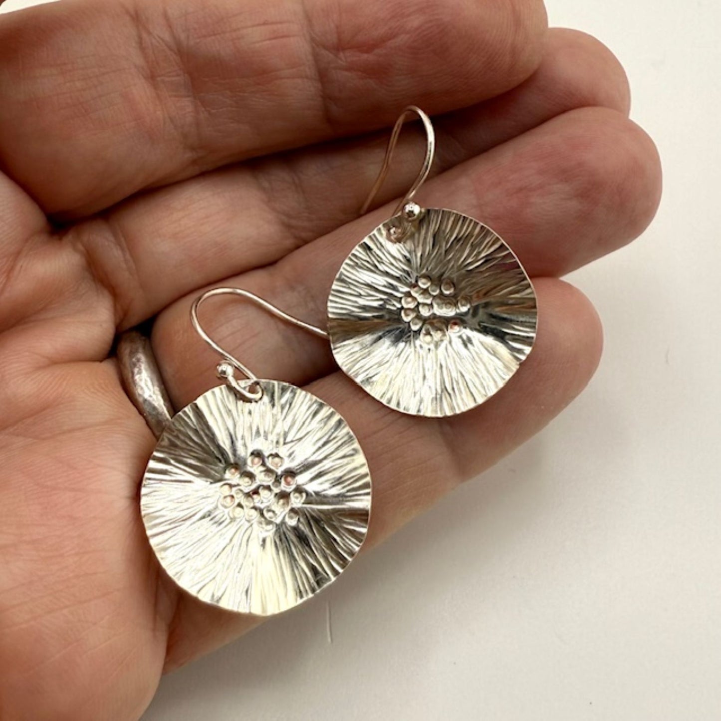 Silver flower earrings held in a hand against a neutral background