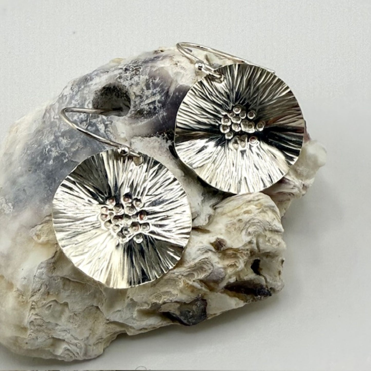 Silver floral earrings on a textured stone surface