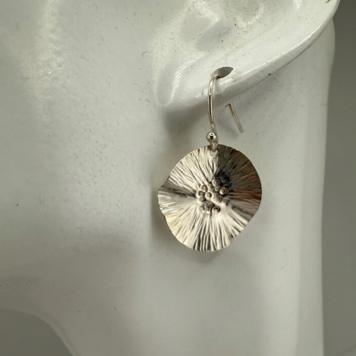 Silver floral earring on a white mannequin ear