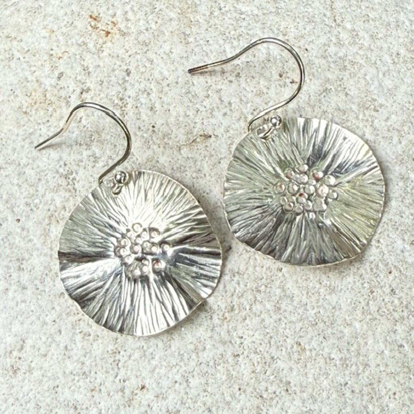 Silver floral earrings on a textured stone surface