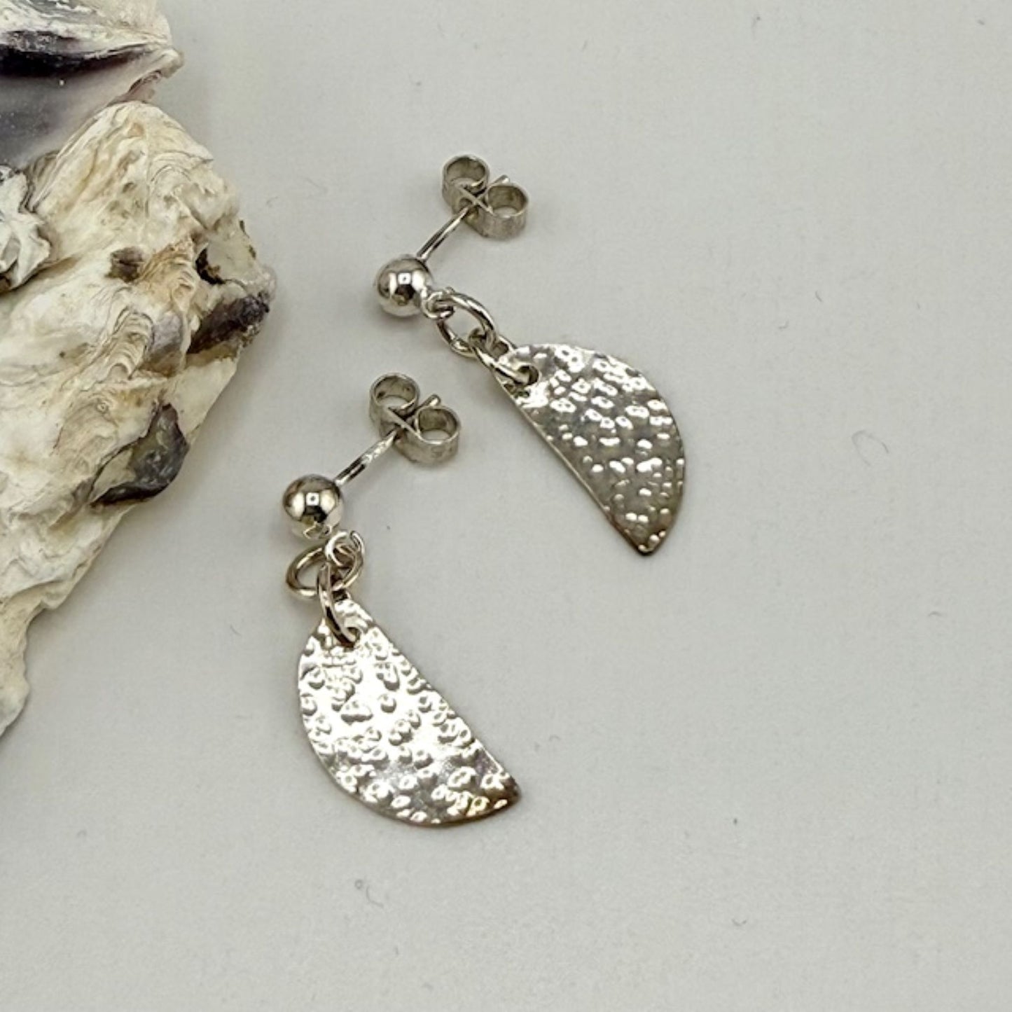 Silver earrings with textured half-circles on a light gray background