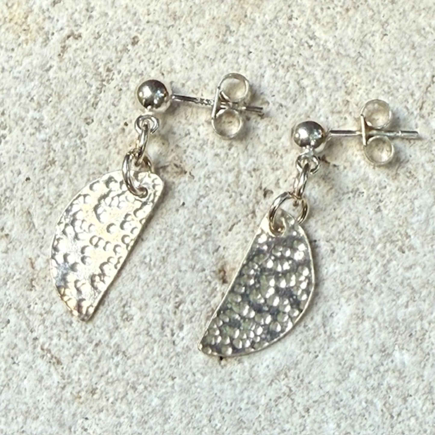 Silver stud earrings with textured half-circles on a light gray background