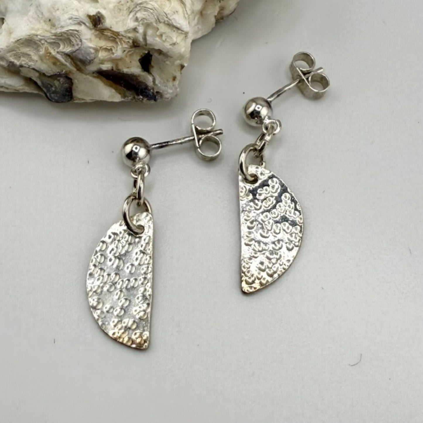 Silver half moon earrings on a light gray surface with a natural rock background.