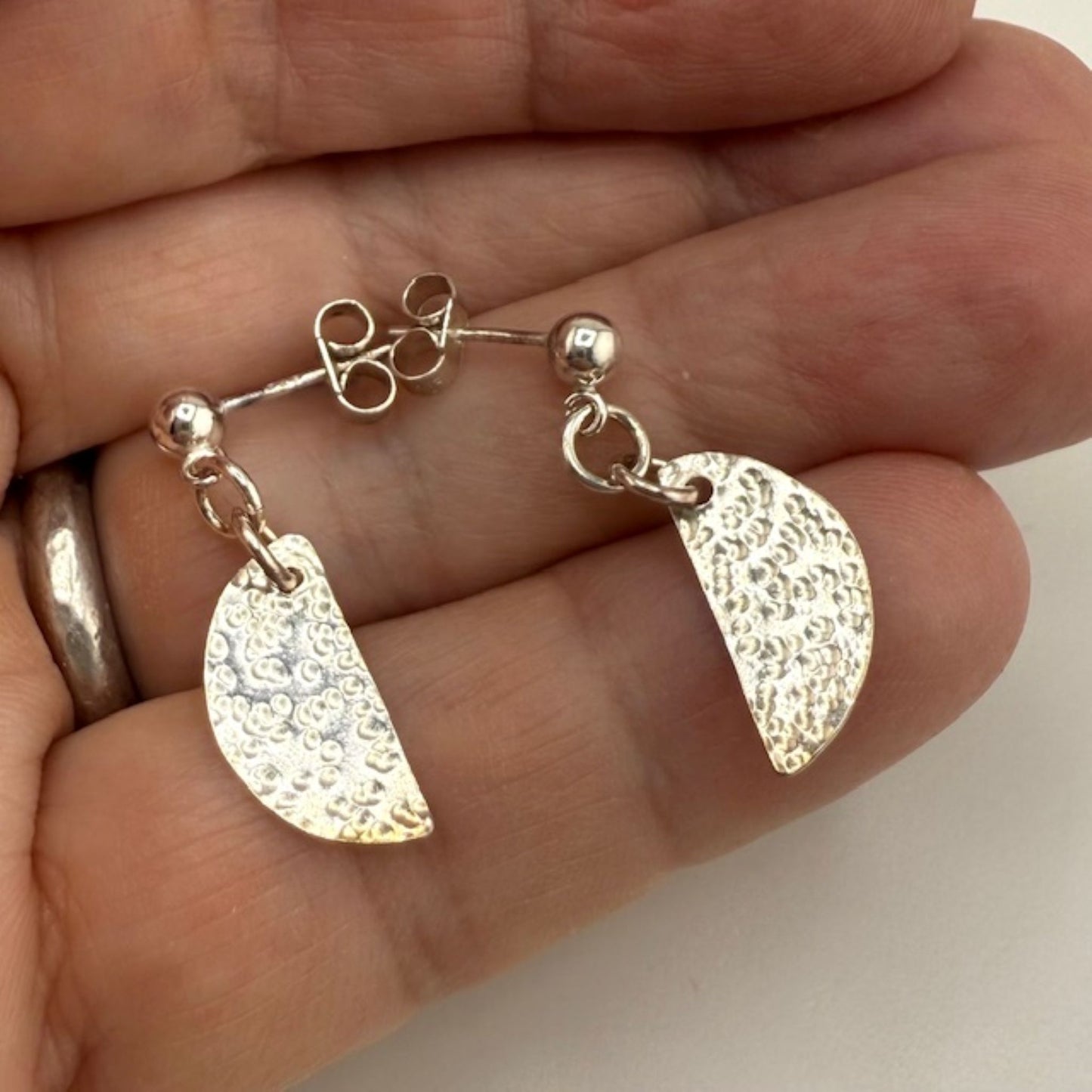 Silver half moon stud earrings held between fingers against a neutral background