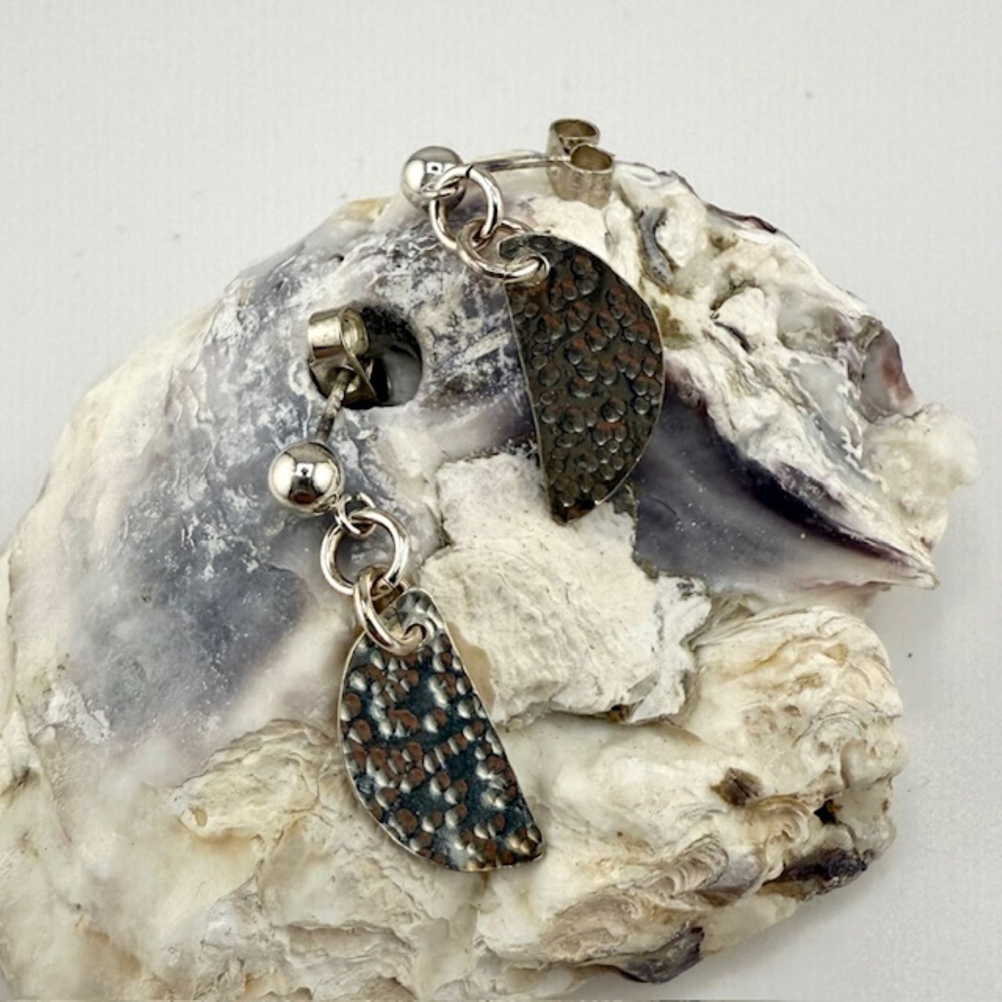 Silver half moon stud earrings on a textured stone surface
