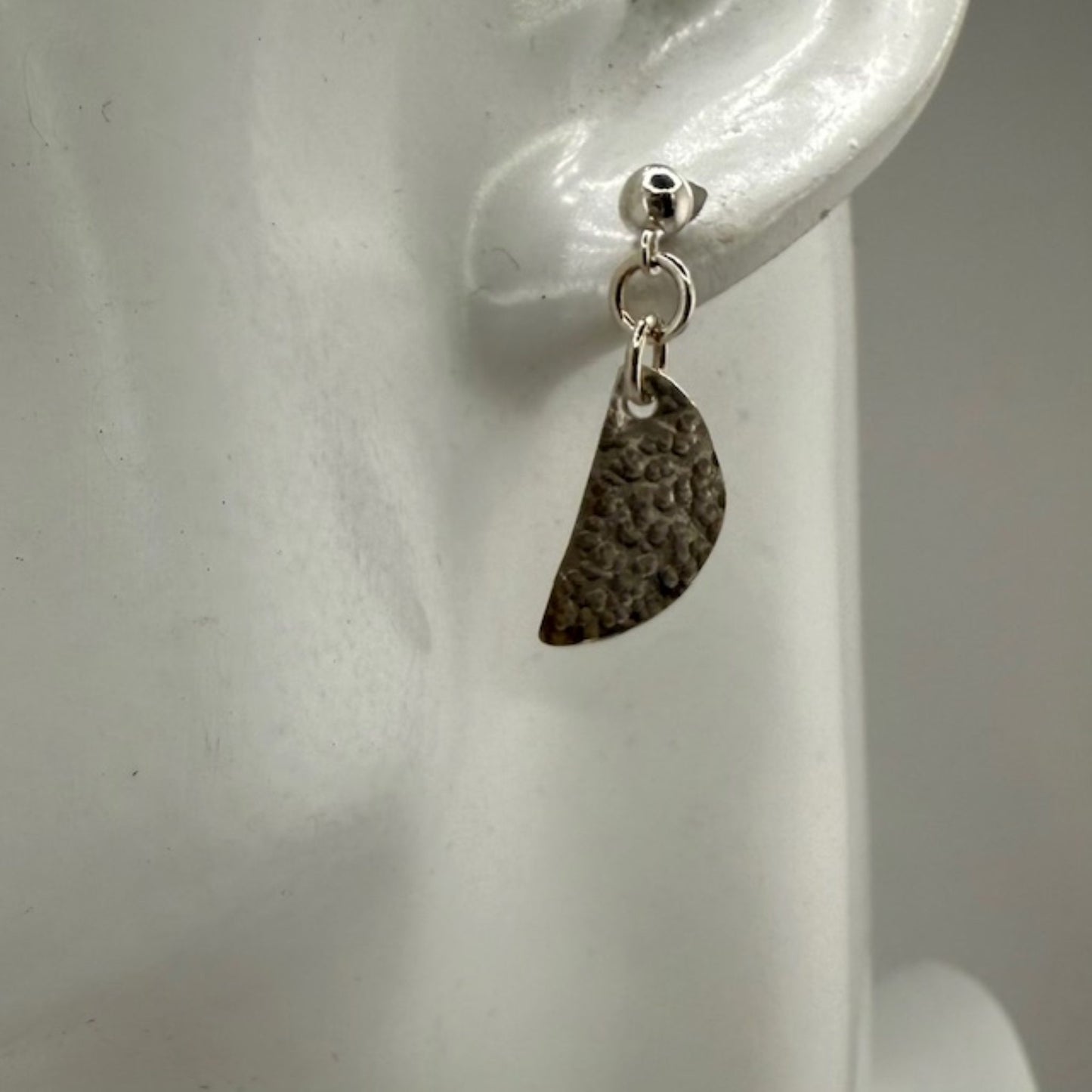 Silver earring with textured half-circle on a mannequin ear.