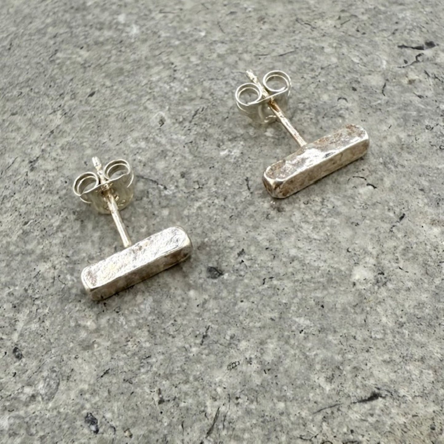 Pair of silver bar stud earrings on a gray concrete surface