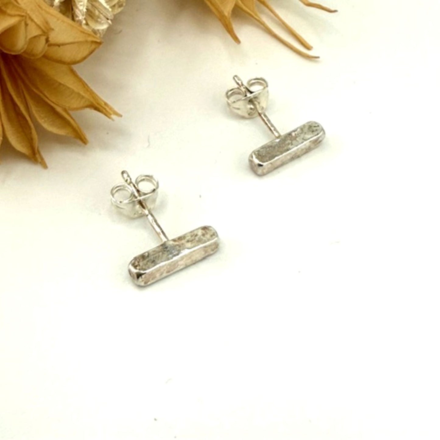 Silver bar stud earrings on a white surface with floral elements.