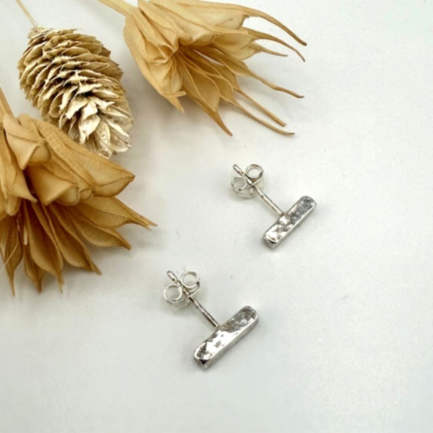 Silver stud bar earrings on a white surface with dried flowers.