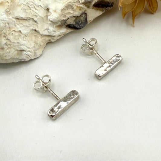 Silver bar stud arrings on a white surface with a natural rock and leaf in the background