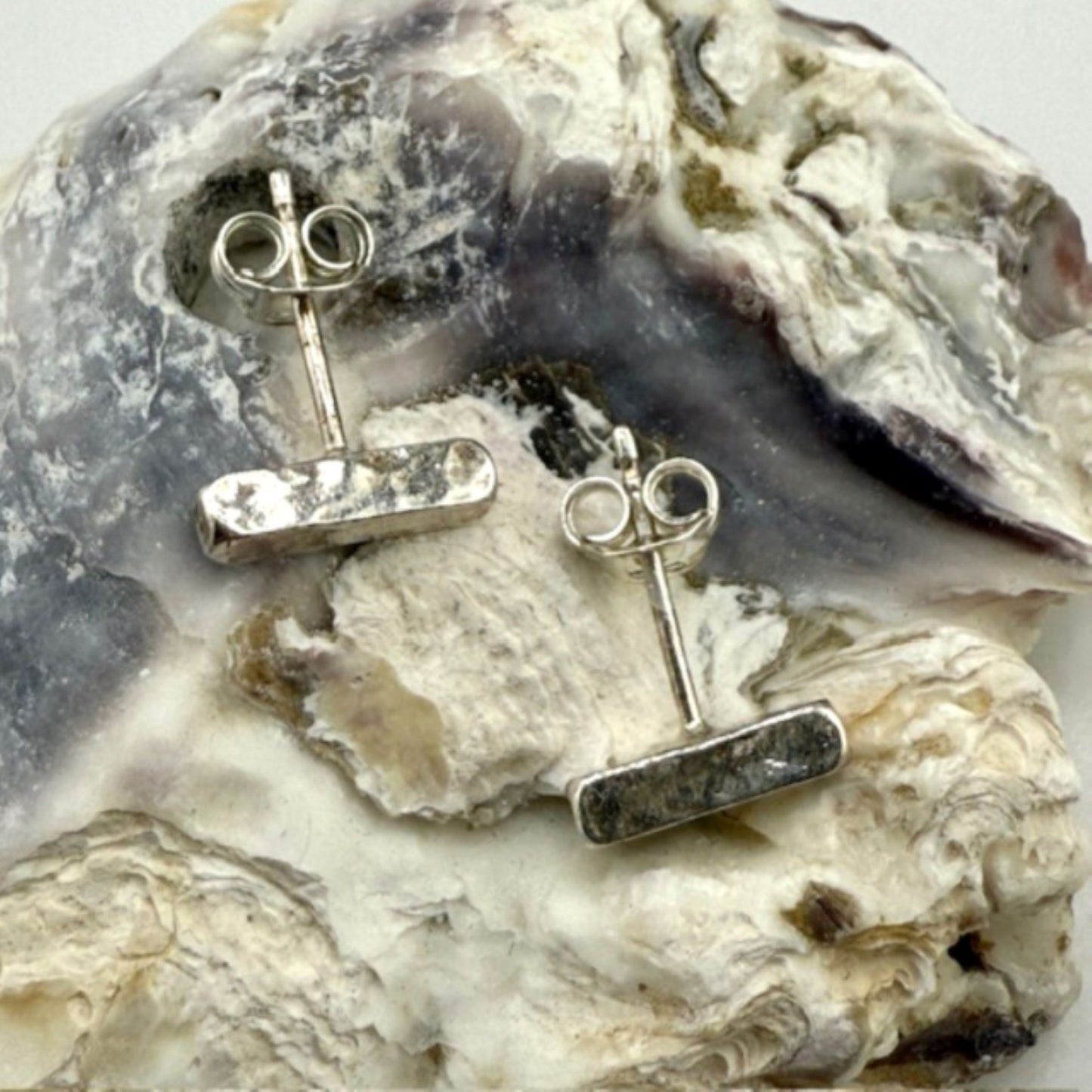 Silver bar stud earrings on a textured oyster shell