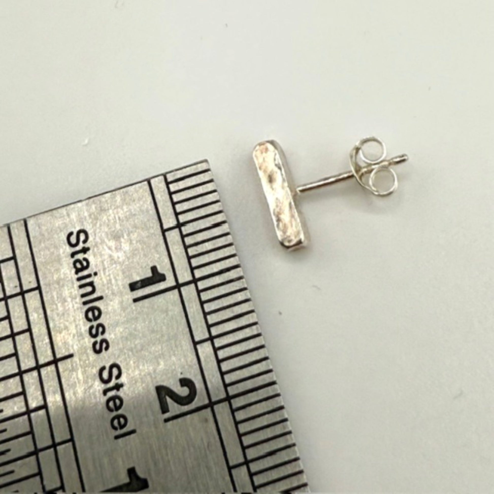 Silver bar stud earrings next to a ruler on a white background