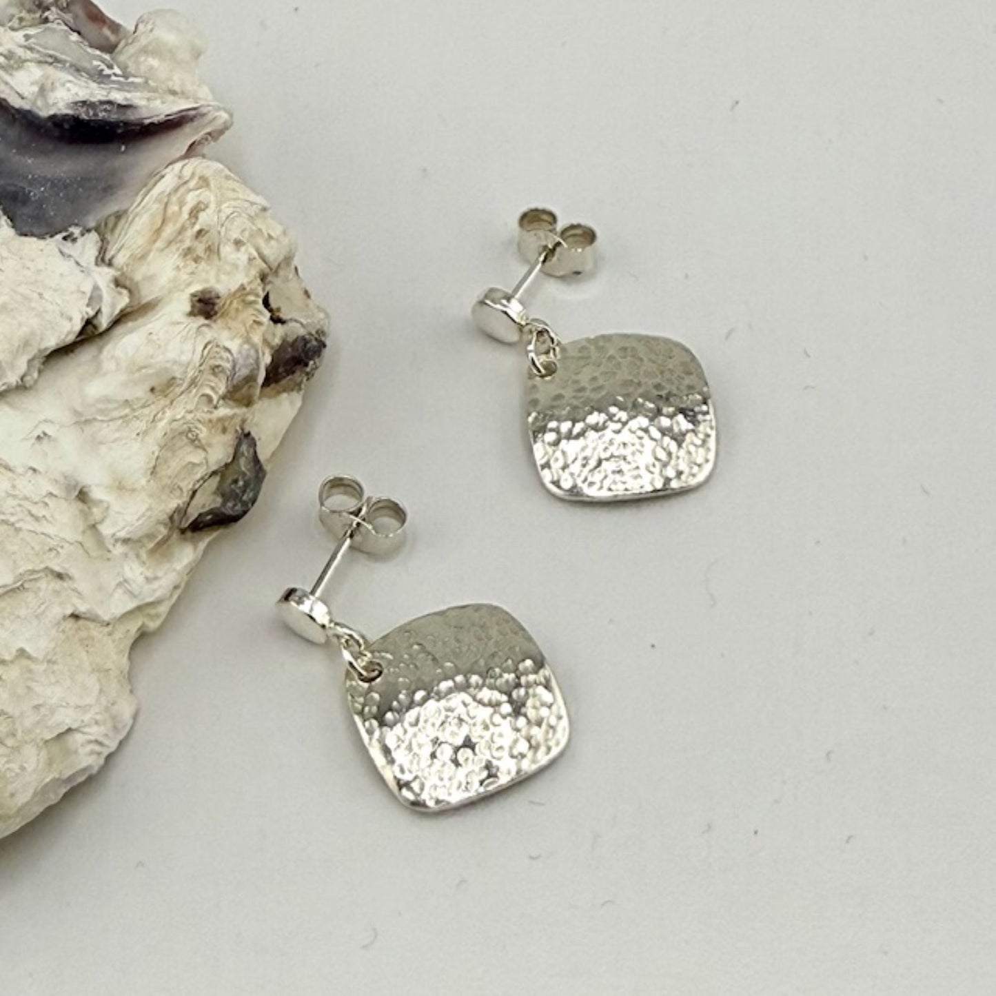 Silver square earrings with textured design on a light gray background