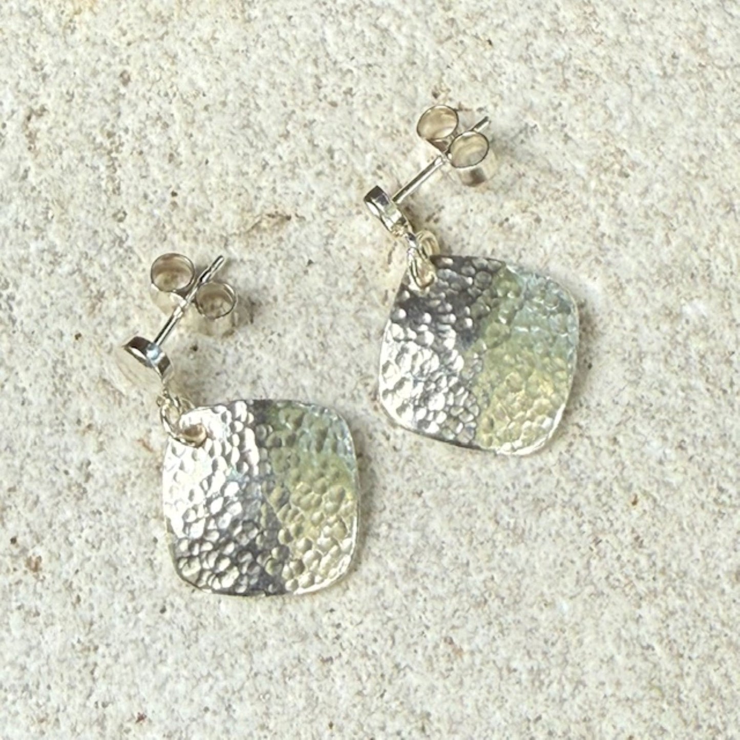 Pair of silver square earrings with textured designs on a stone background