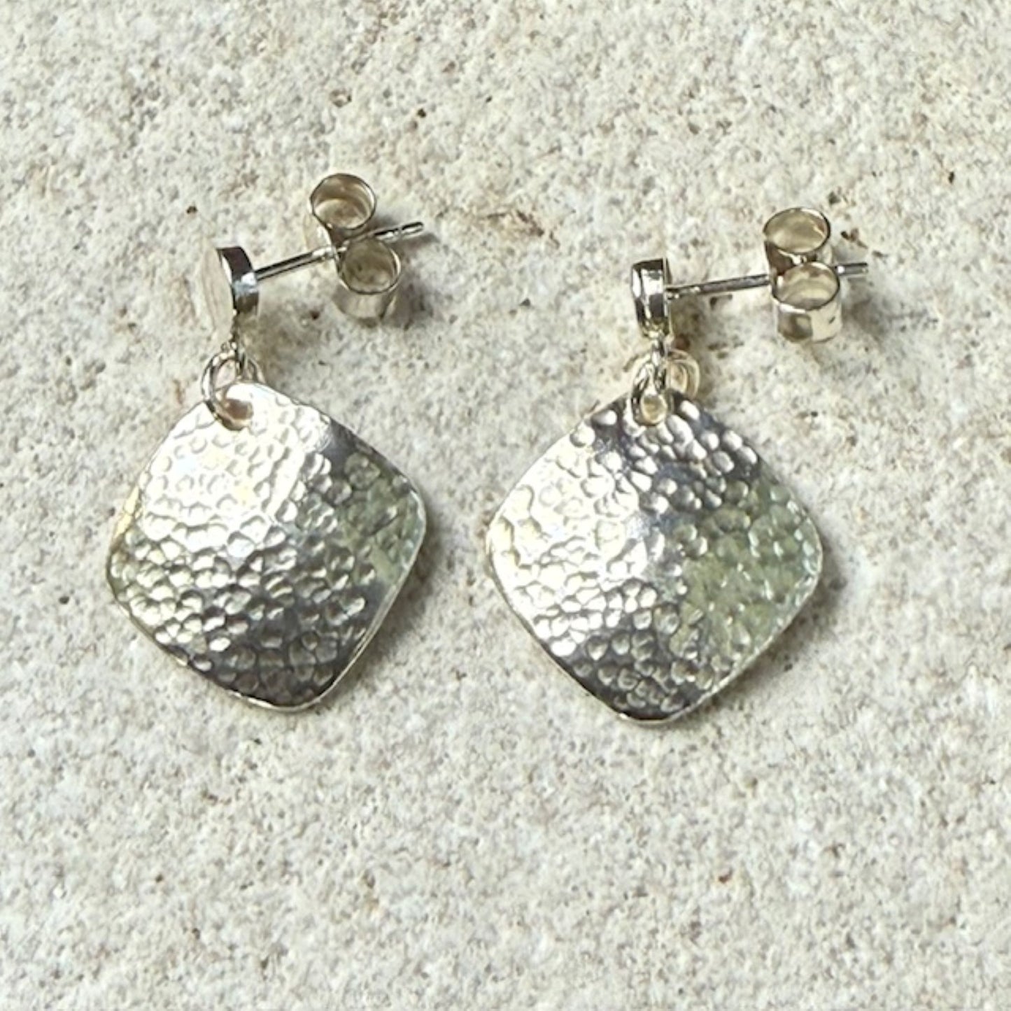 Pair of silver square earrings with textured square pendants on a light gray surface