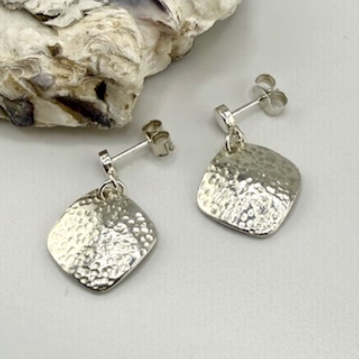 Silver square earrings on a light gray surface with a stone background