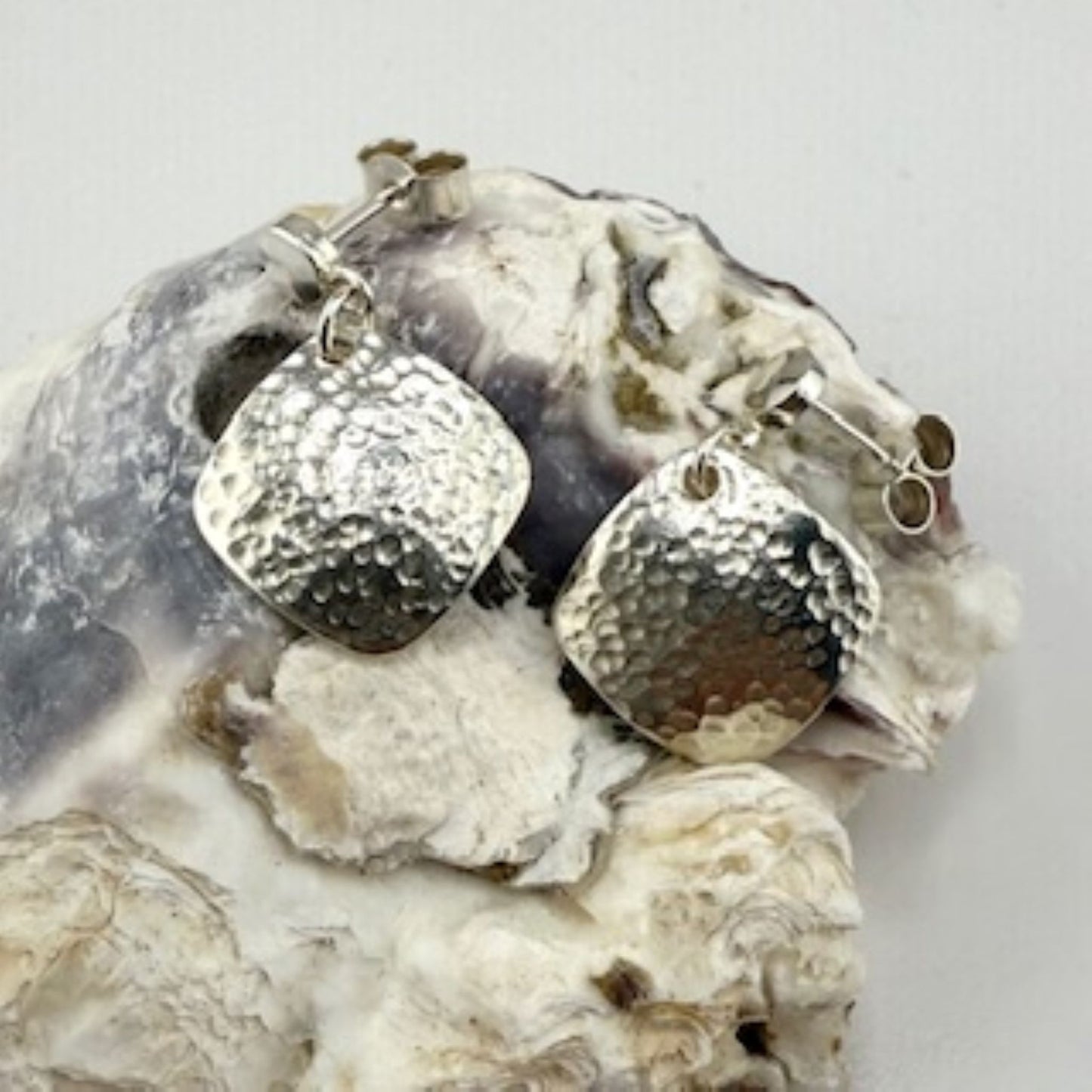 Silver square earrings on a textured stone surface