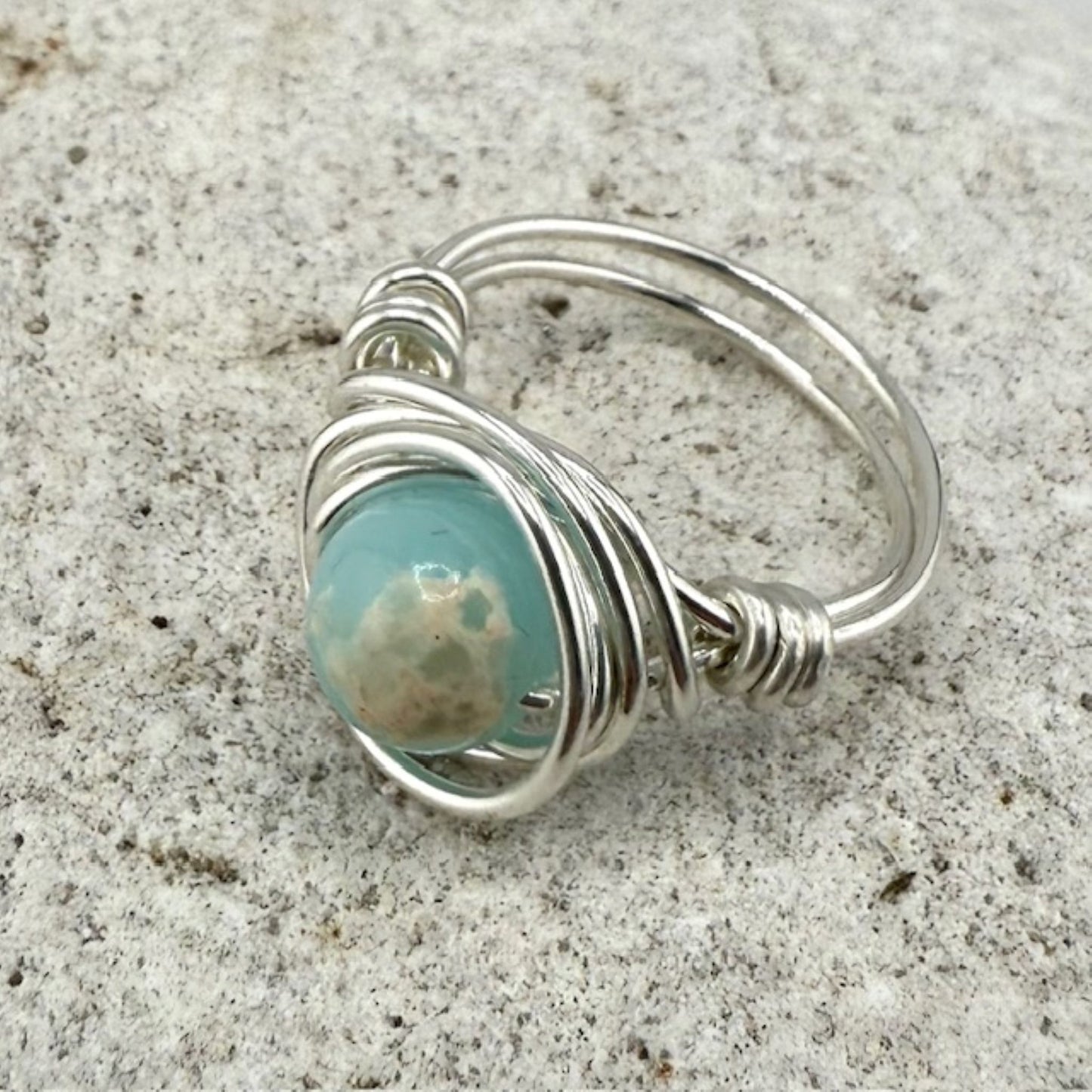 Silver wire-wrapped ring with a blue-green gemstone on a textured surface