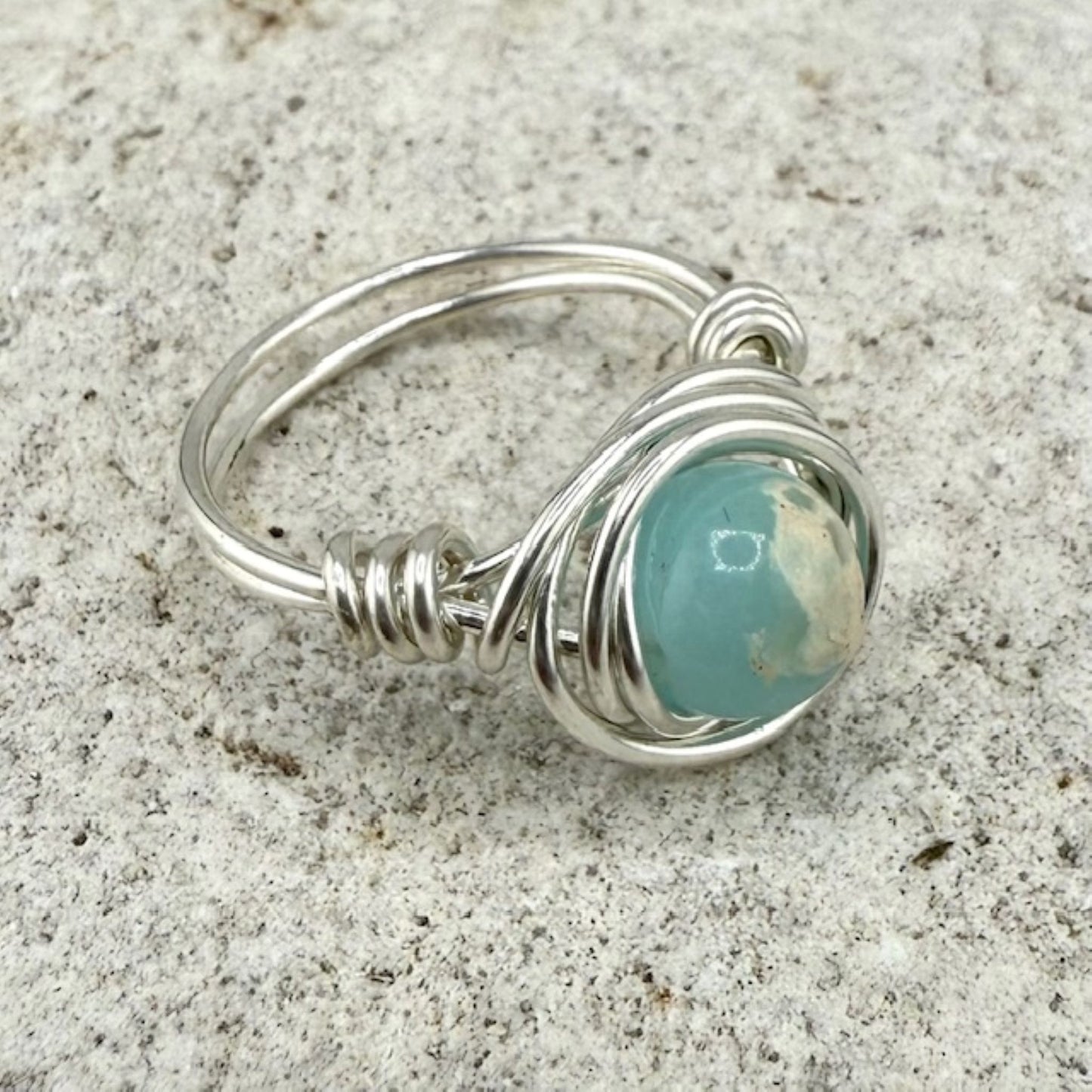 Silver wire-wrapped ring with a aqua stone on a stone background