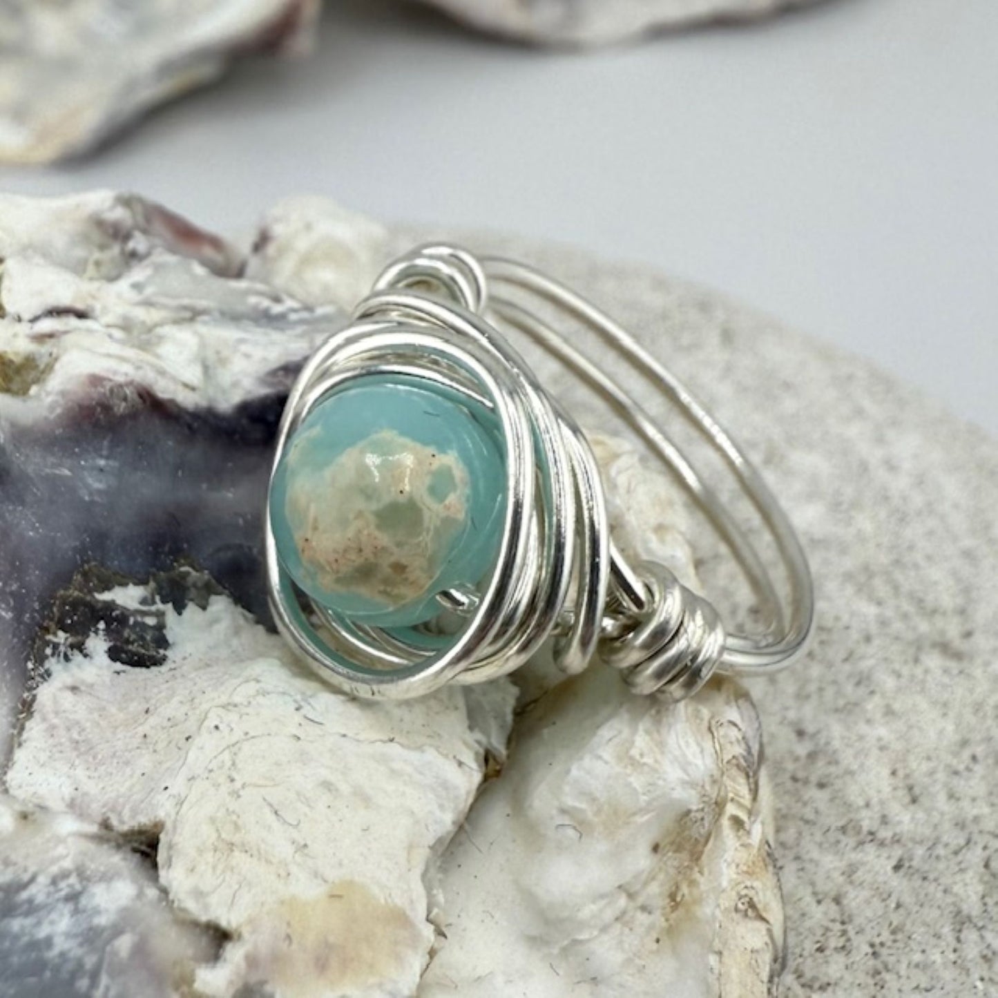 Silver ring with a sea blue green stone on a textured surface