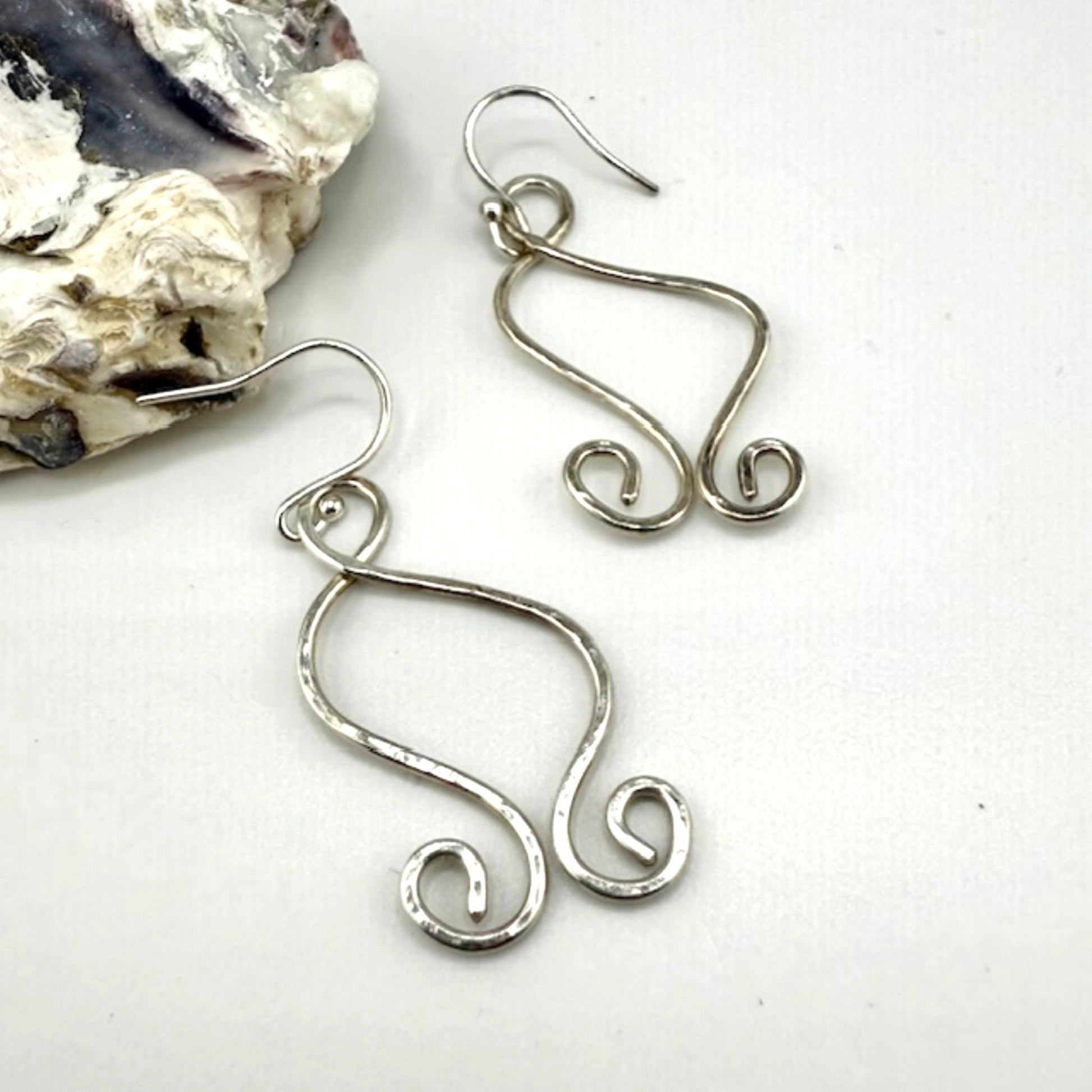 Silver wire earrings on a white background with a stone object.