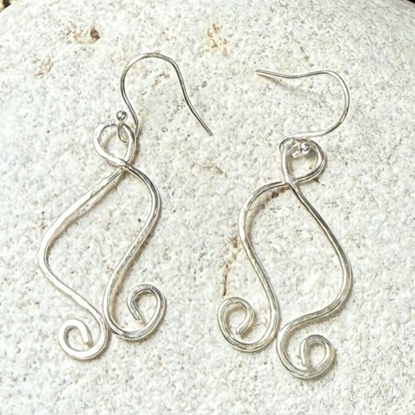 Silver wire earrings on a textured white stone surface