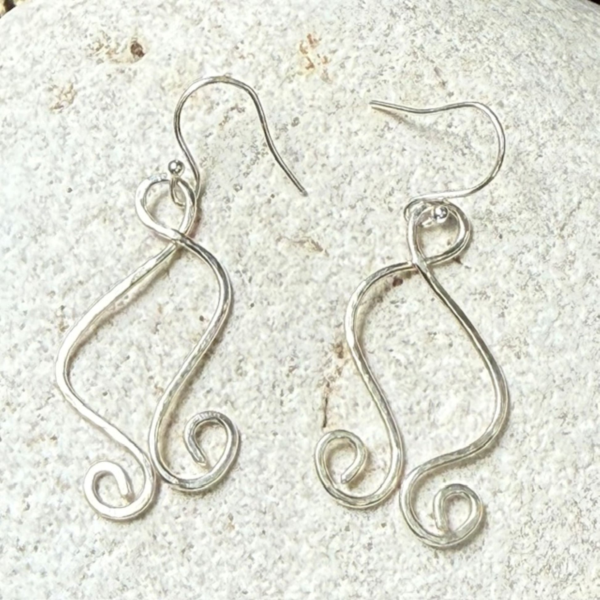 Silver wire earrings on a textured white stone surface