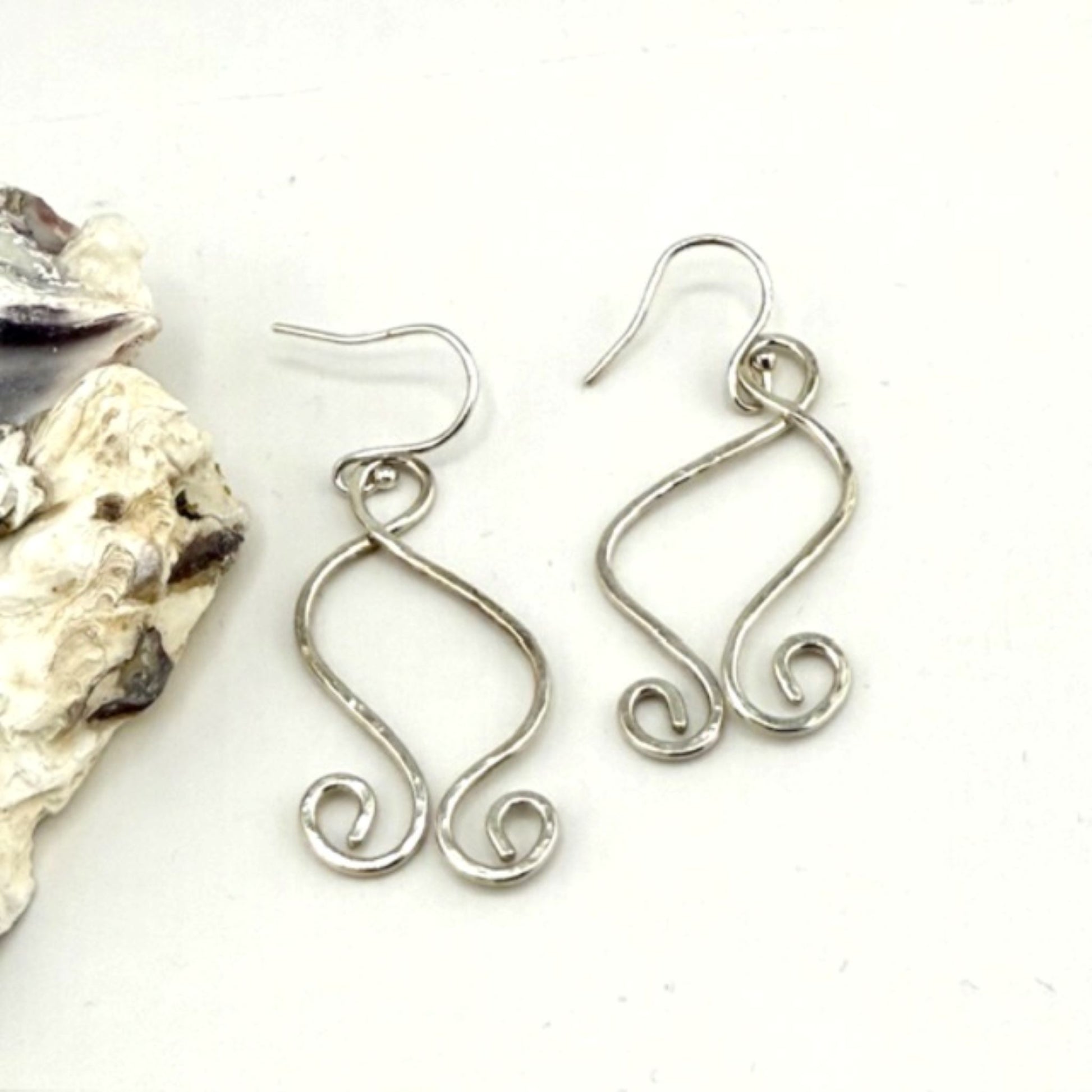 Silver wire earrings on a white background with a shell.