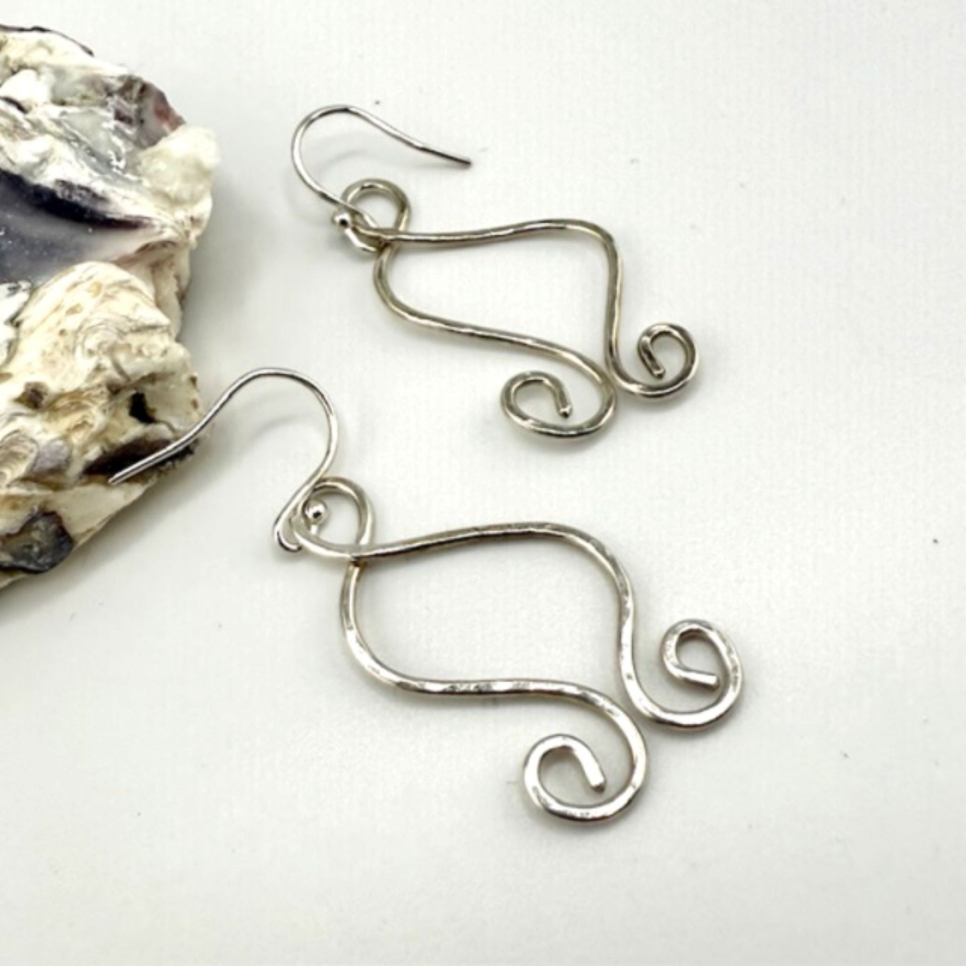 Silver wire earrings on a white surface with a shell in the background