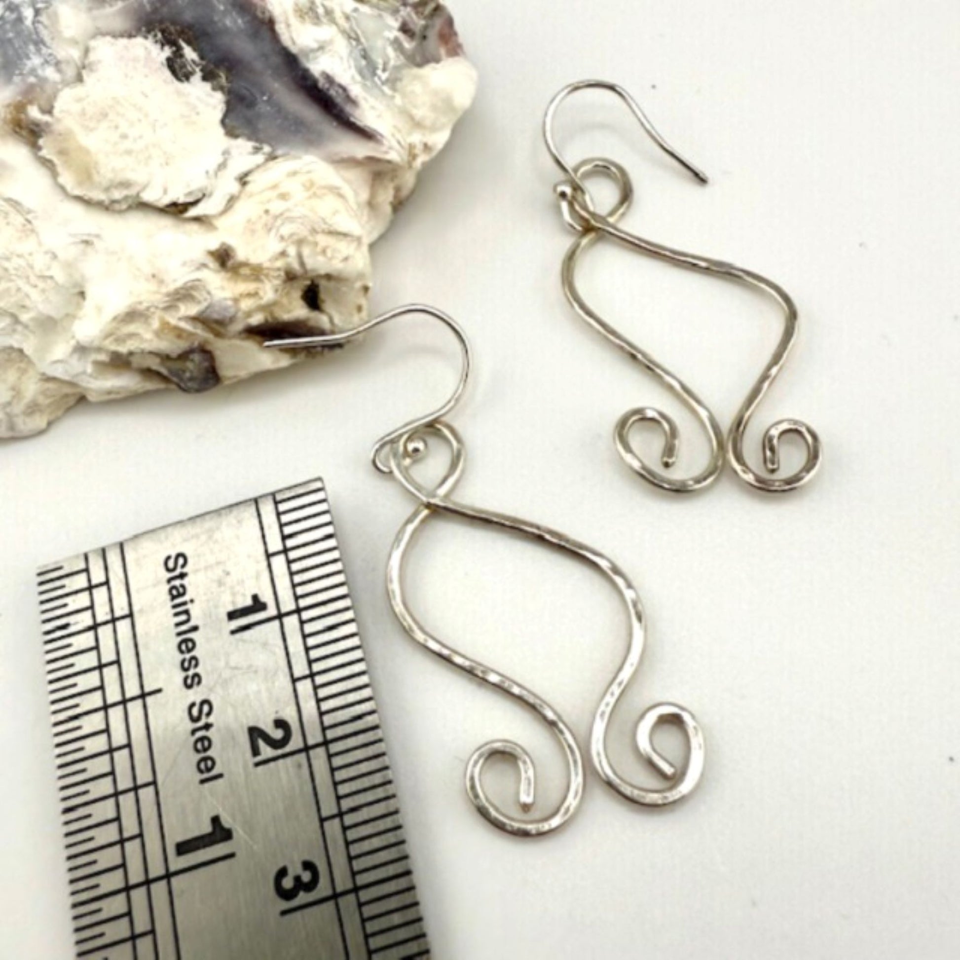 Silver wire earrings with a measuring ruler for scale on a white background
