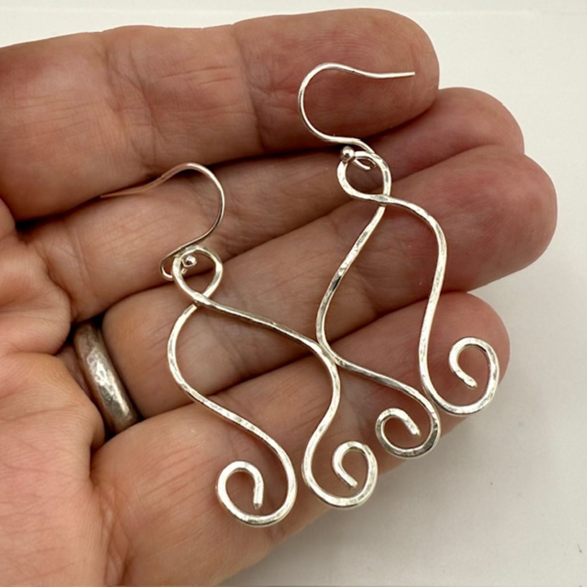 Silver wire earrings held in a hand against a white background