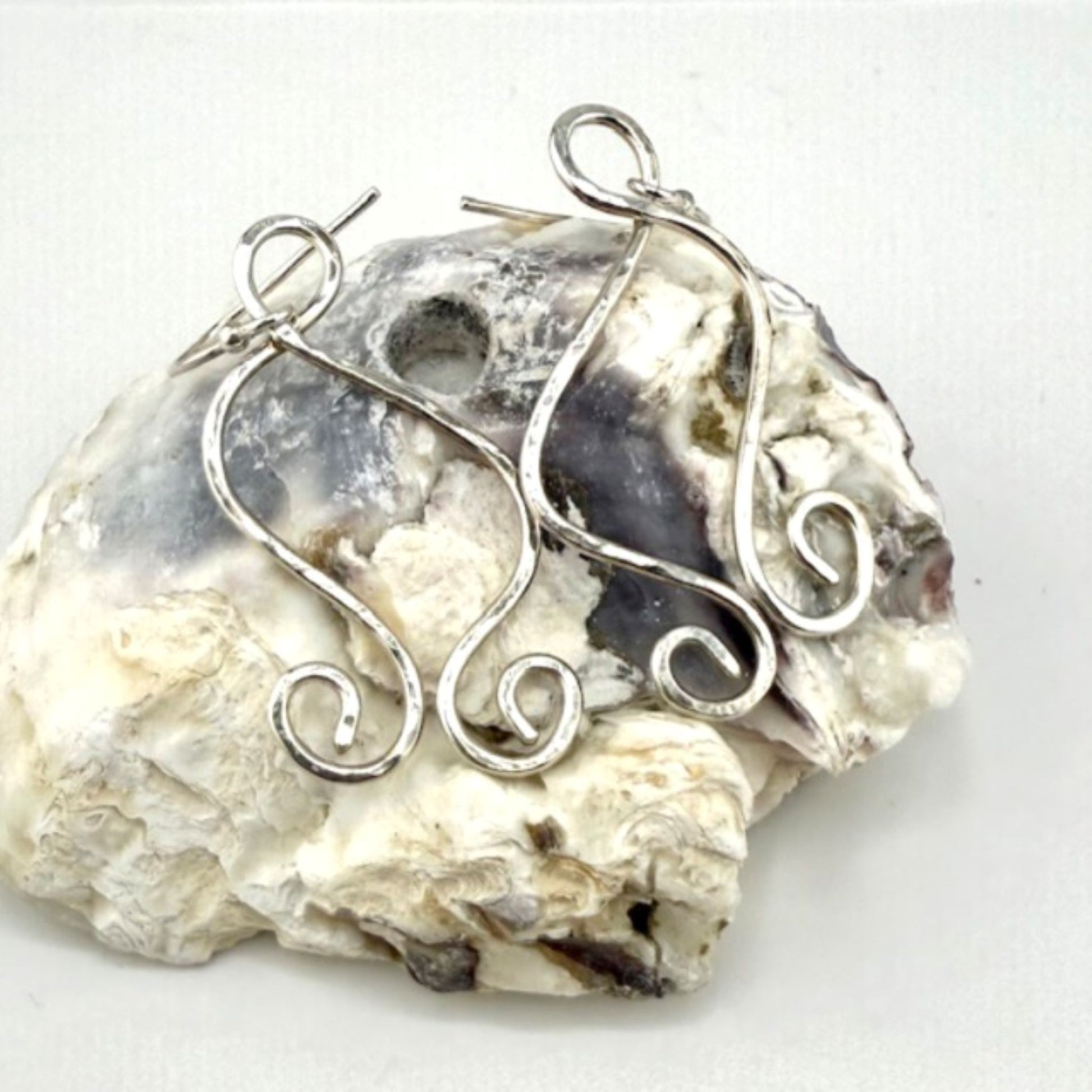 Silver wire earrings on a rough stone surface