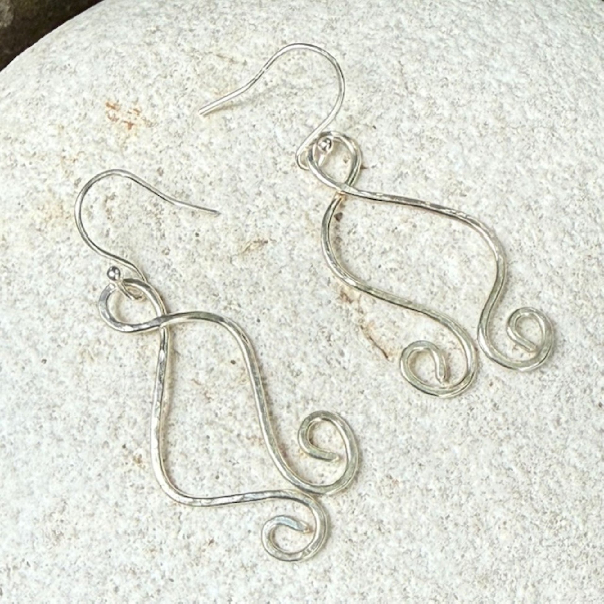 Silver wire earrings on a textured white stone surface