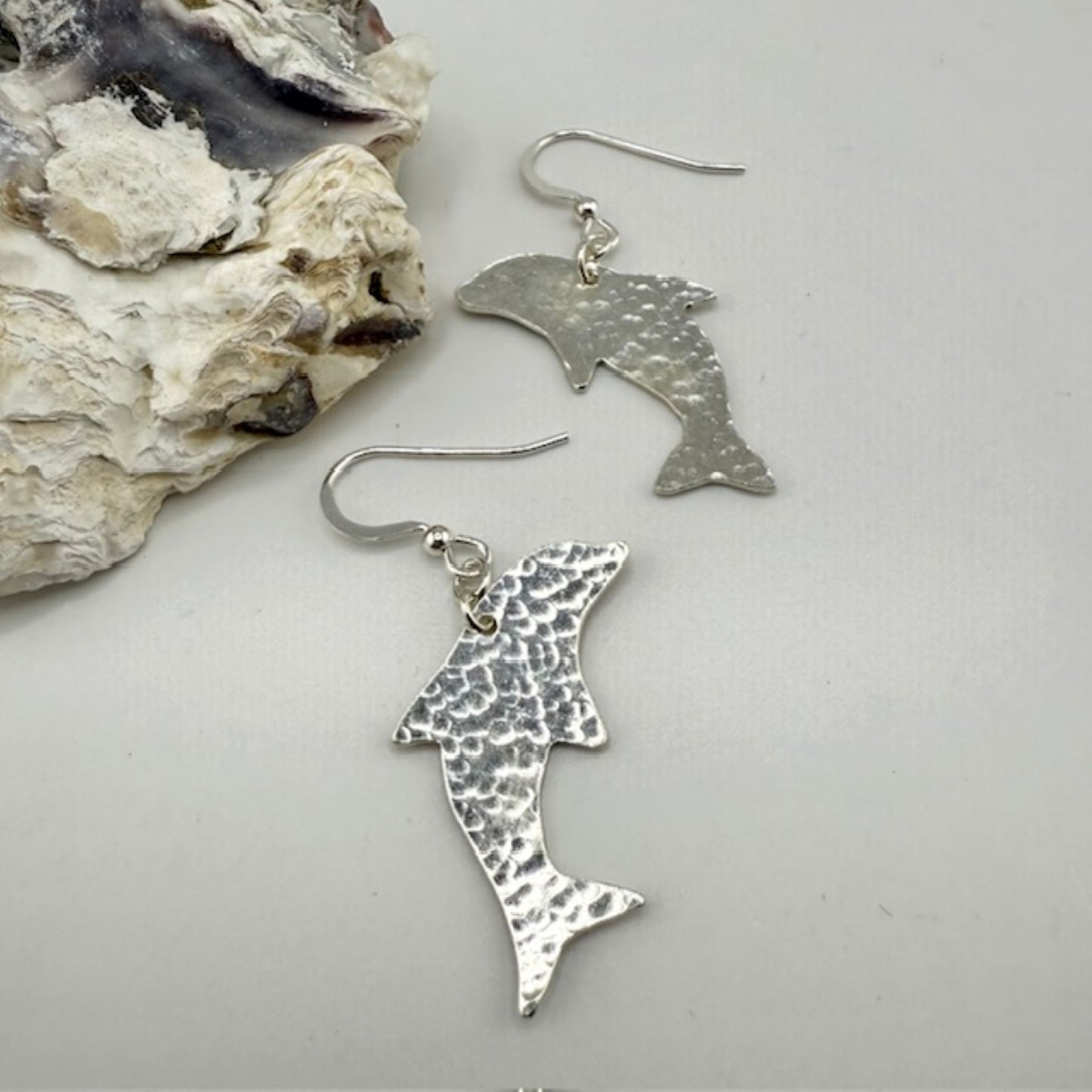 Silver dolphin earrings on a light gray surface with a shell background