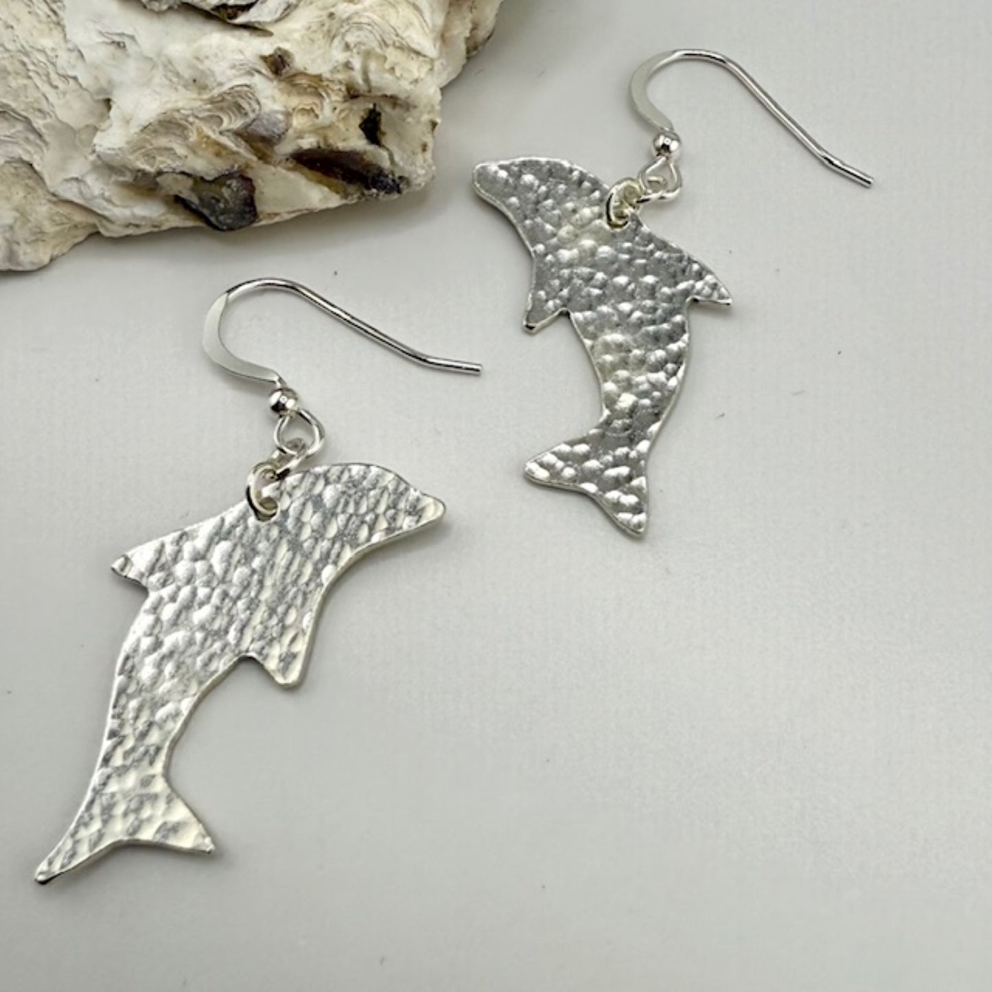 Silver dolphin-shaped earrings on a light gray background