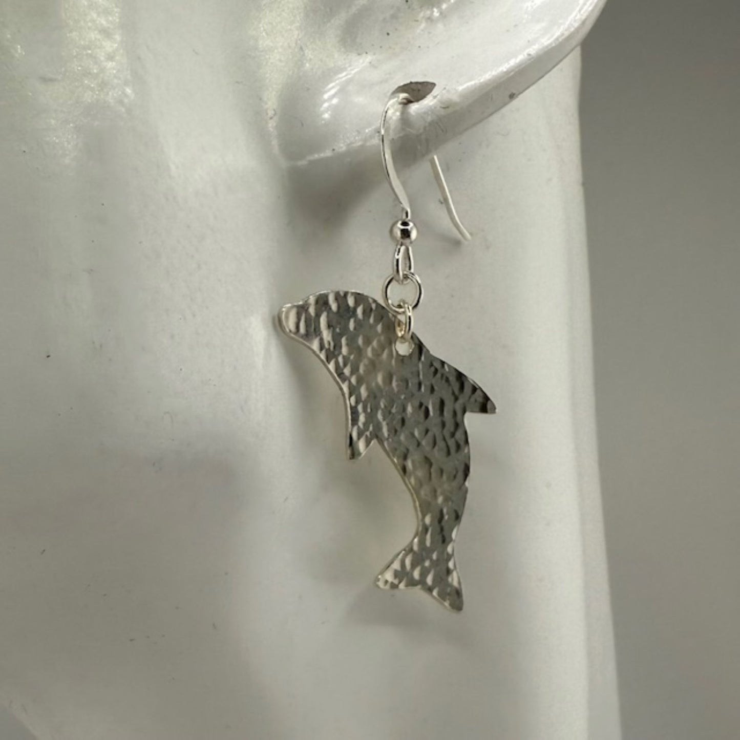 Silver dolphin earrings on a white earring stand.