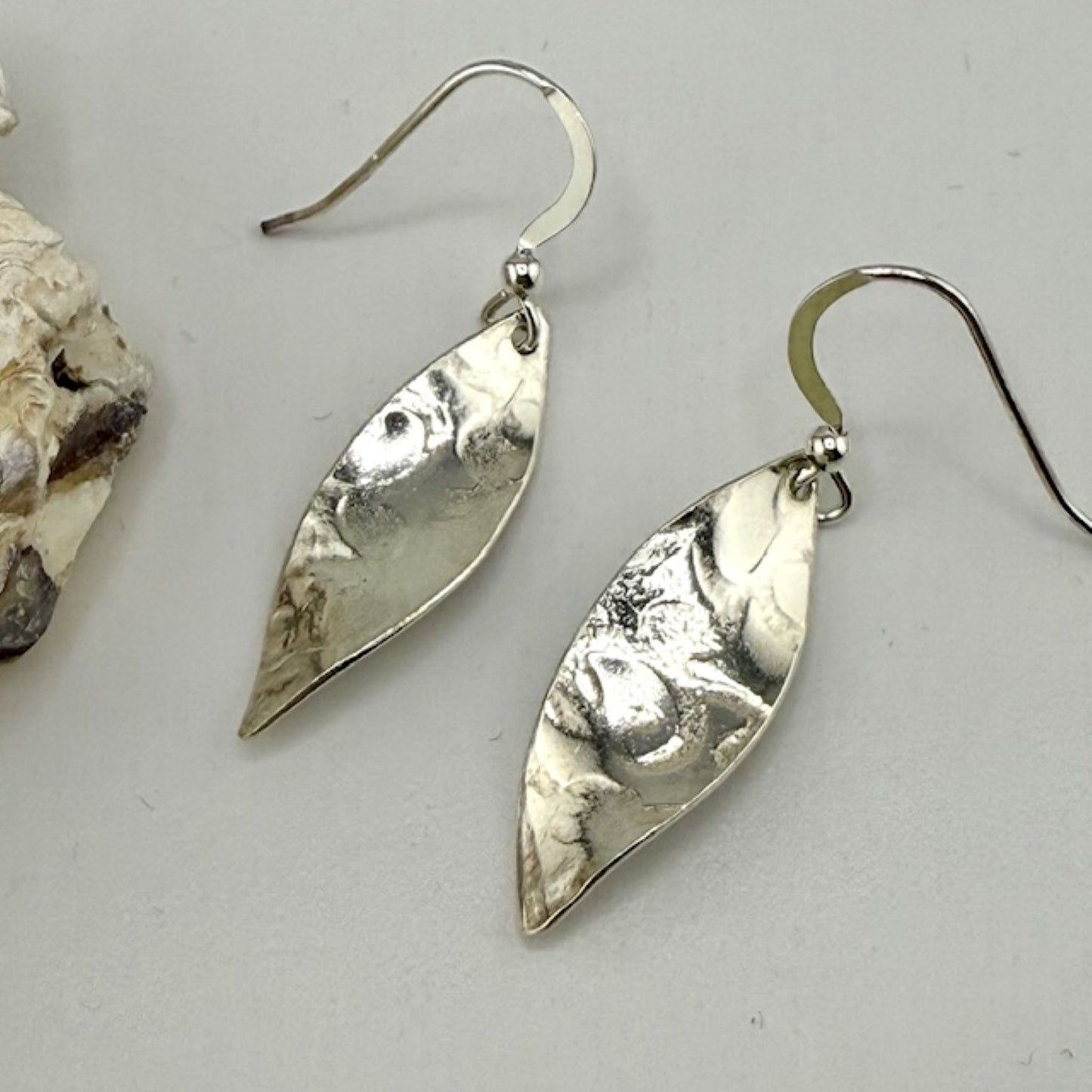 Silver leaf-shaped earrings on a light gray background