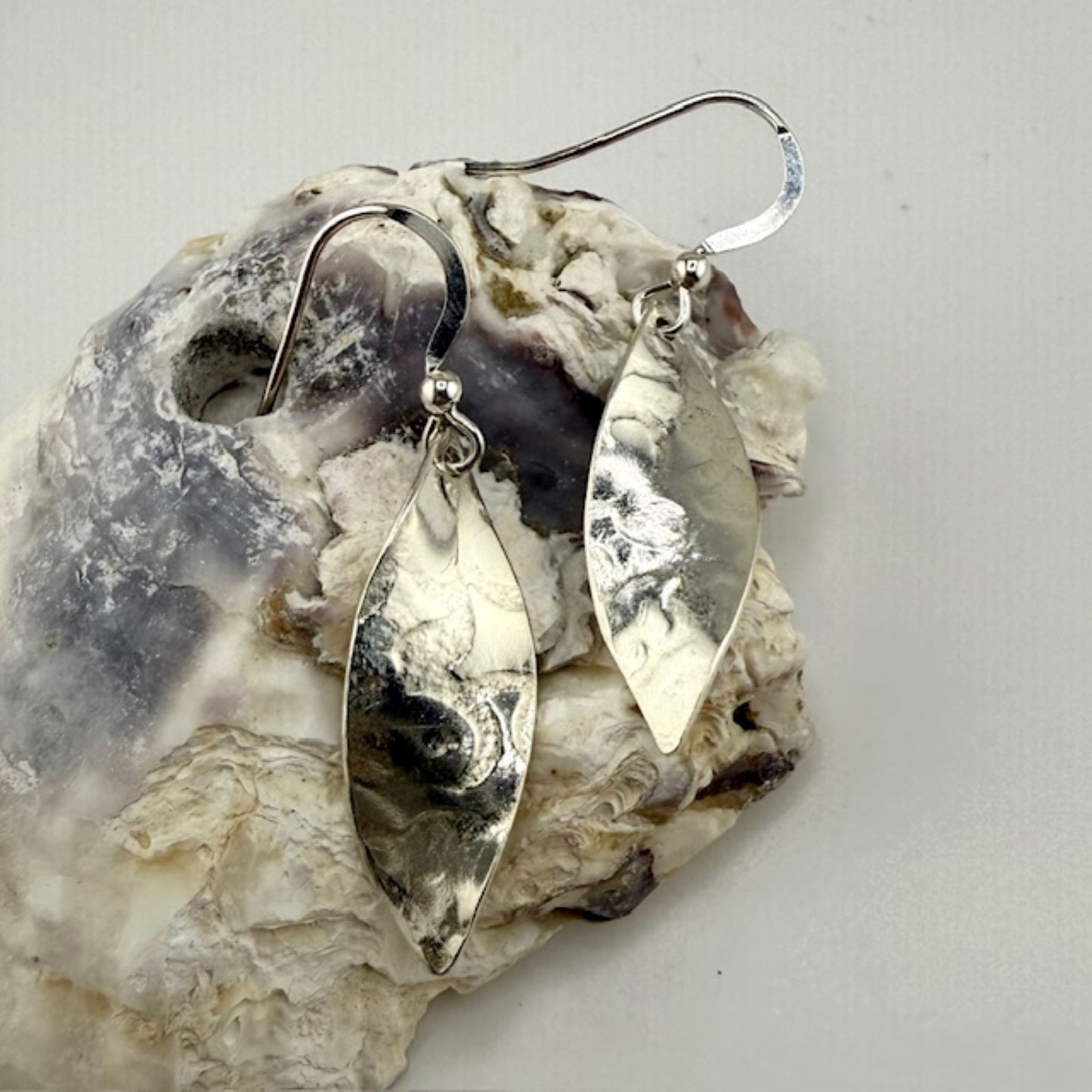 Silver leaf earrings on a textured stone surface