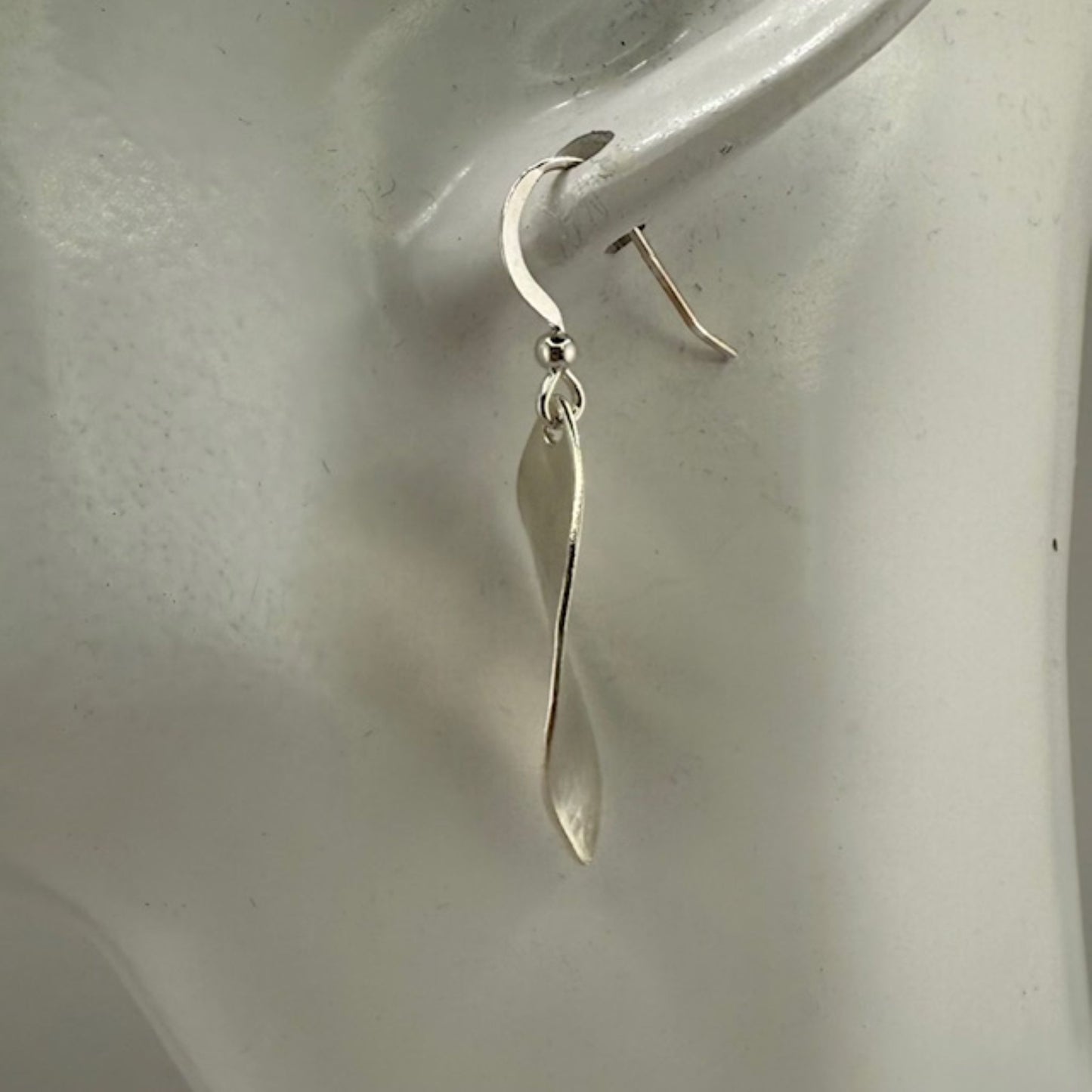 Silver leaf earring on a mannequin ear against a plain background