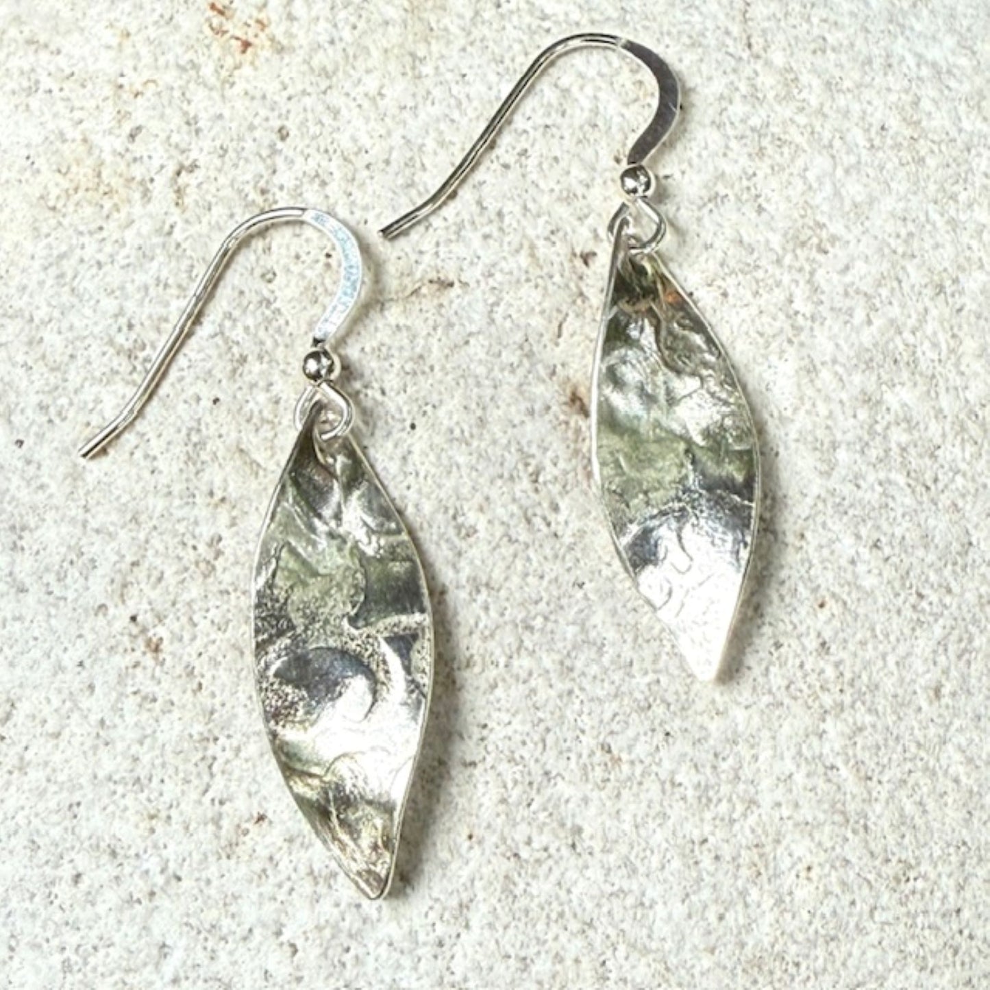 Silver leaf-shaped earrings on a textured stone surface