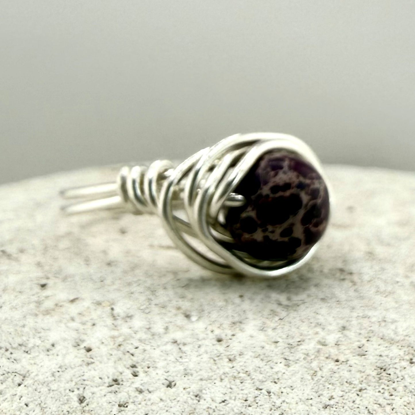 Silver wire-wrapped ring with a Purple Jasper gemstone on a textured surface