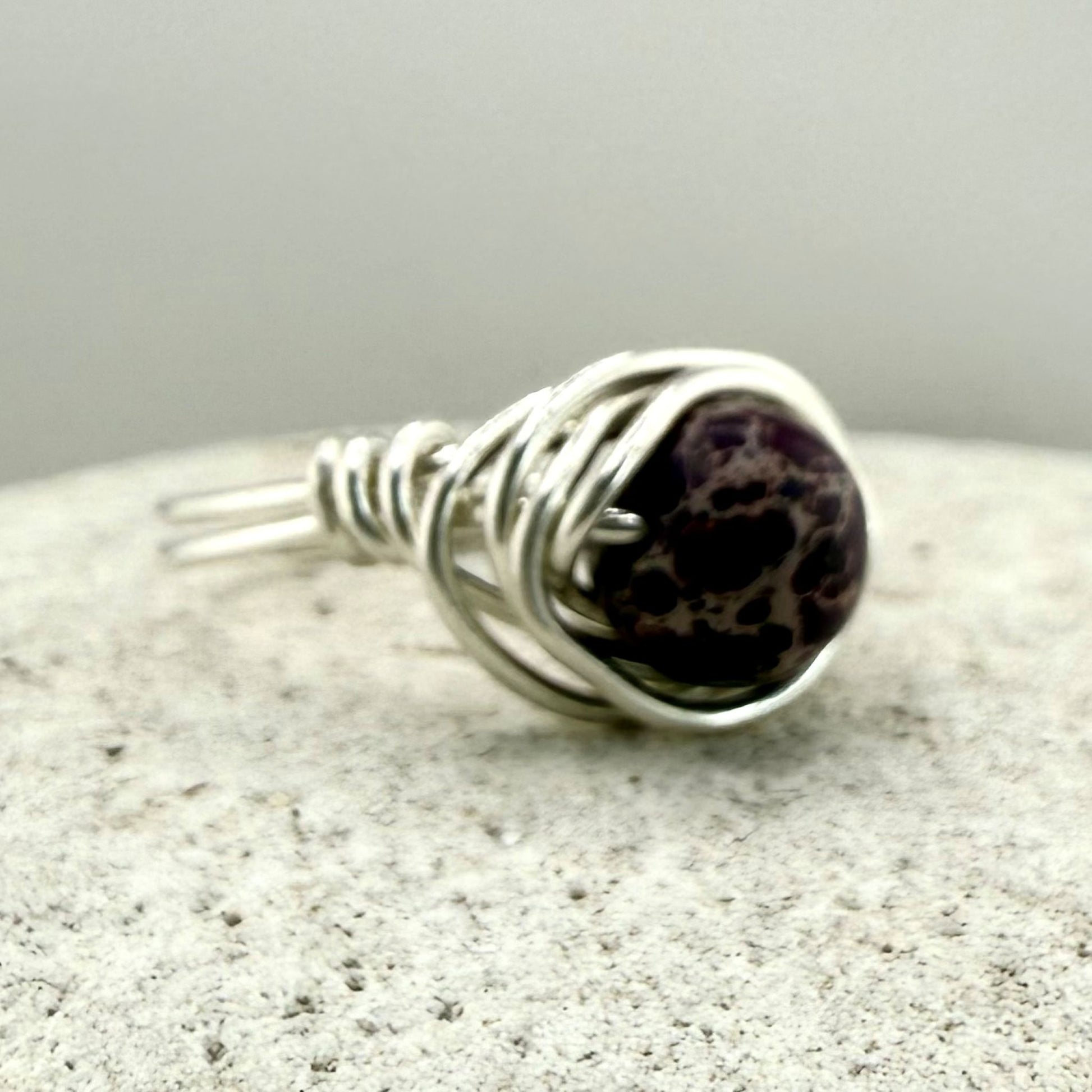 Silver wire-wrapped ring with a Purple Jasper gemstone on a textured surface