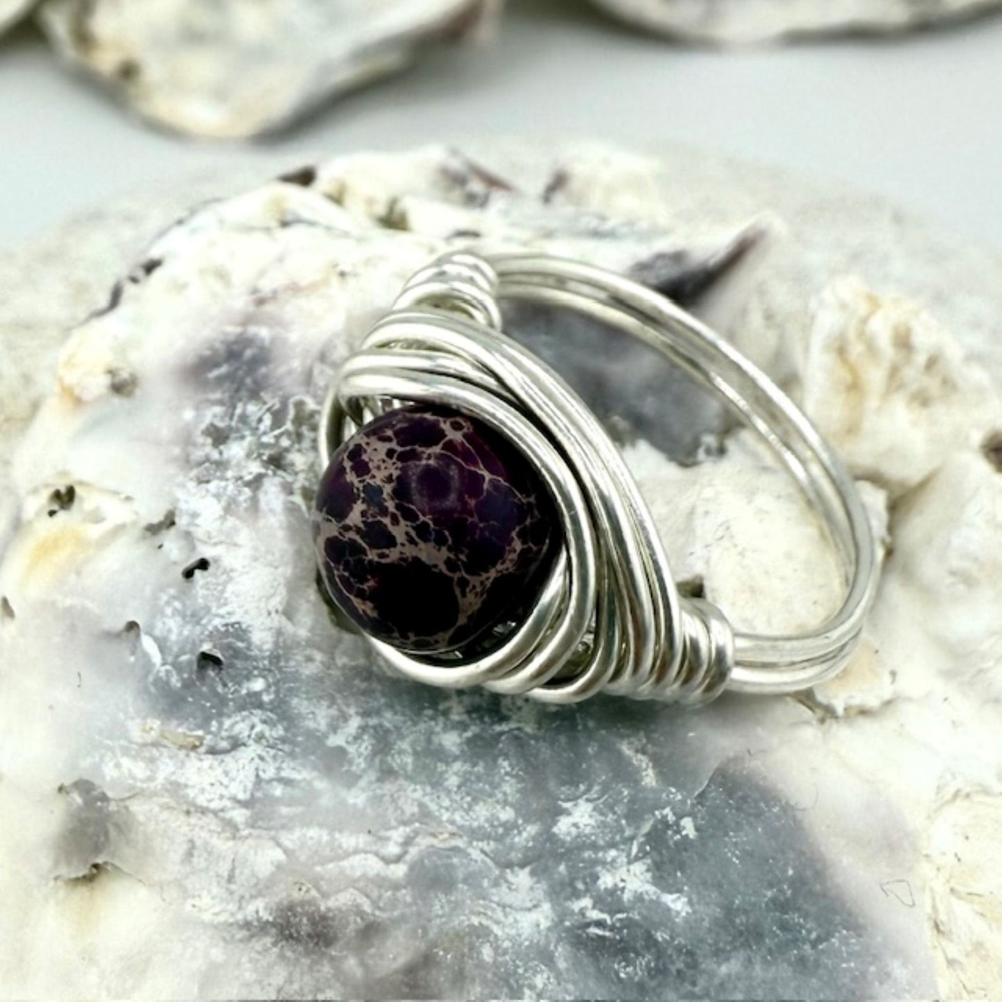 Silver wire-wrapped ring with a purple jasper gemstone on a textured stone surface