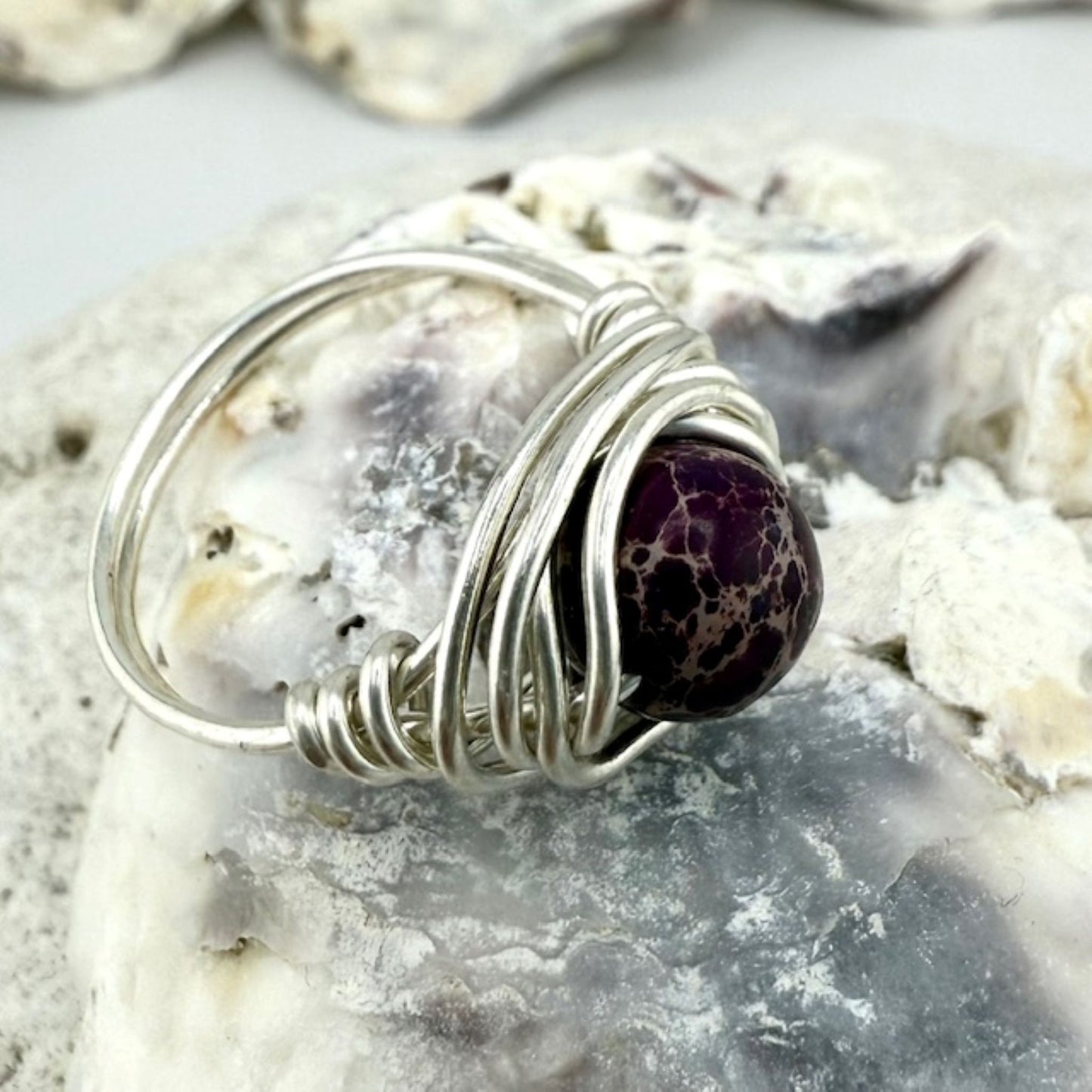 Silver wire-wrapped ring with a purple jasper gemstone on a textured surface