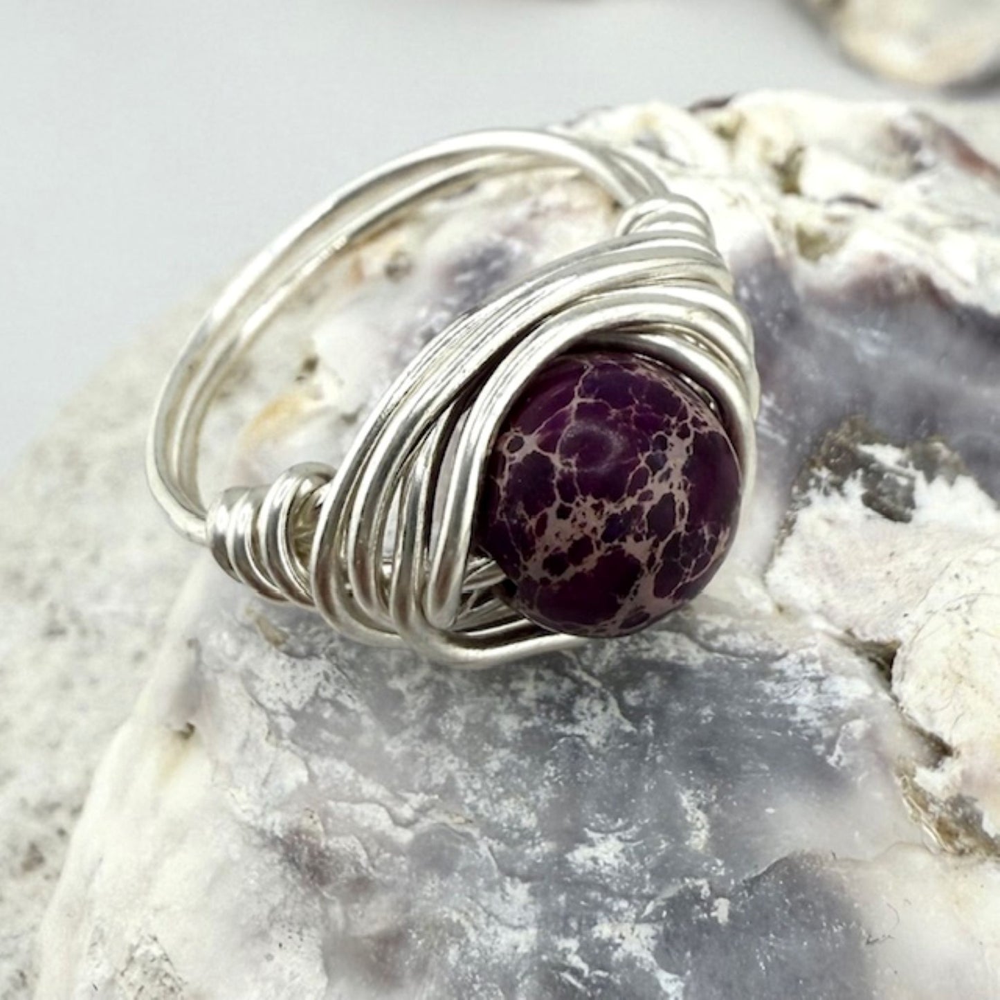 Silver wire-wrapped ring with a purple gemstone on a textured stone background