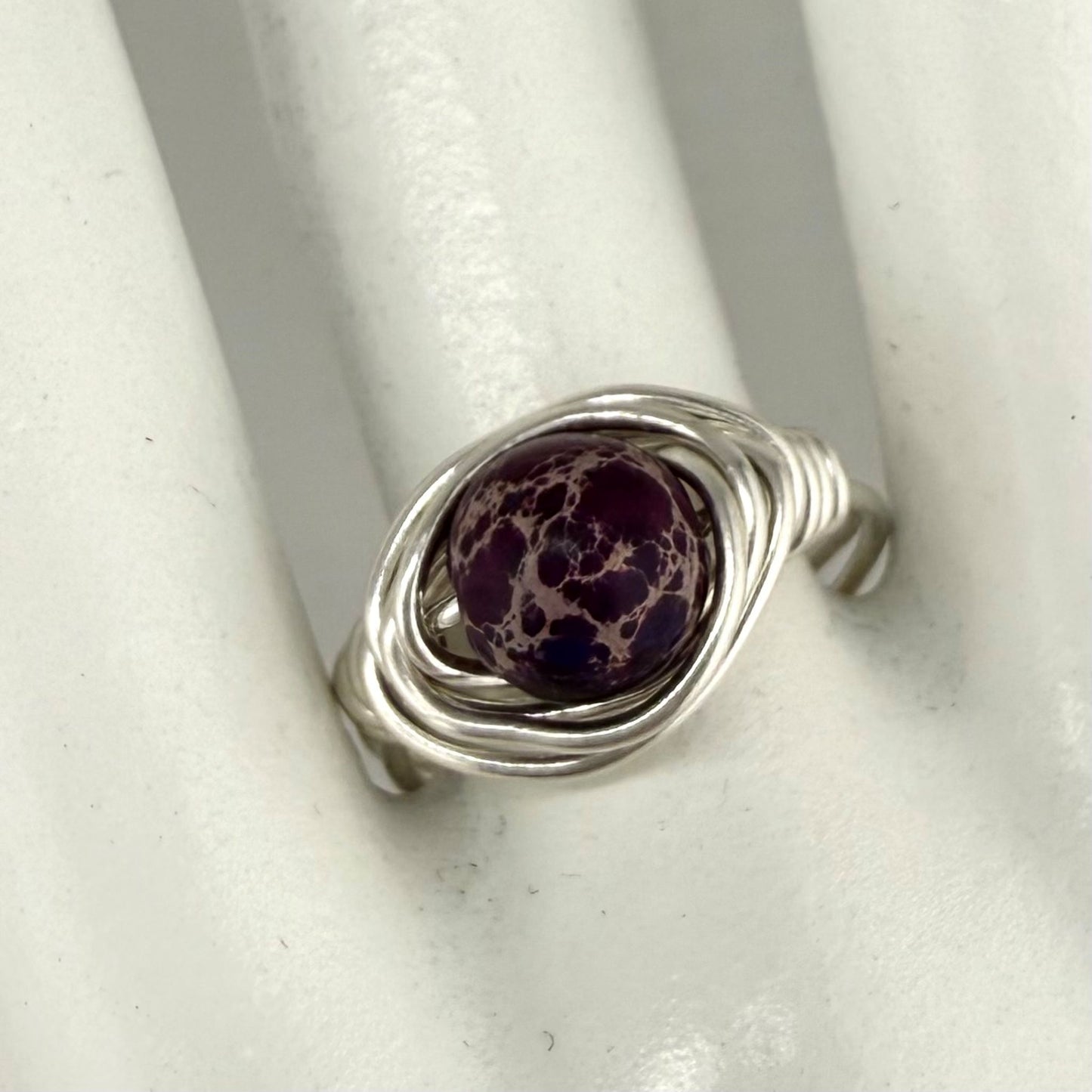 Silver ring with a purple speckled stone on a white marble hand display