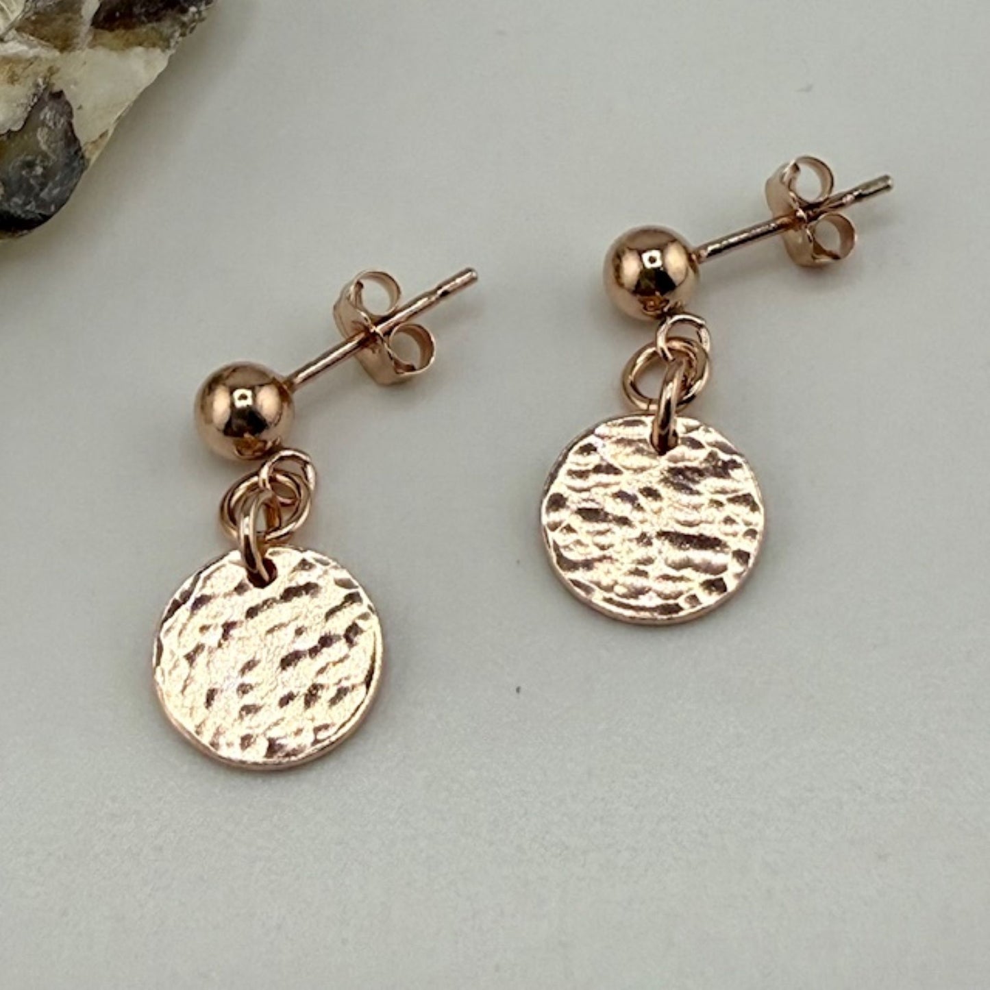Rose gold stud earrings with round, textured discs on a light gray background